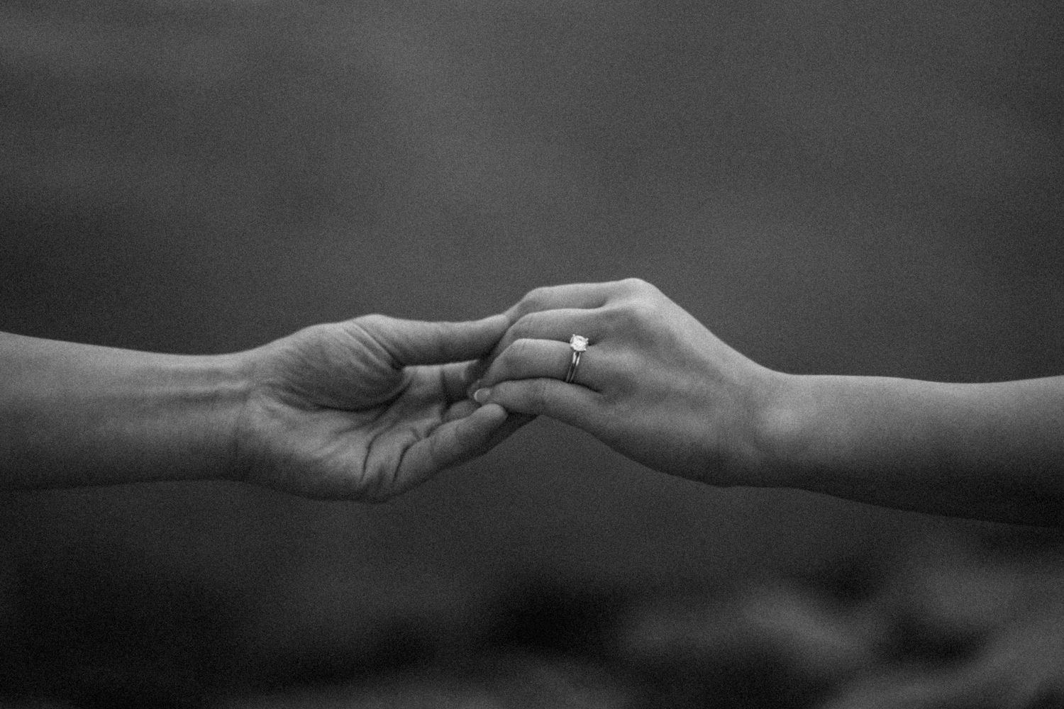 Close-up of hands reaching toward each other in black and white.