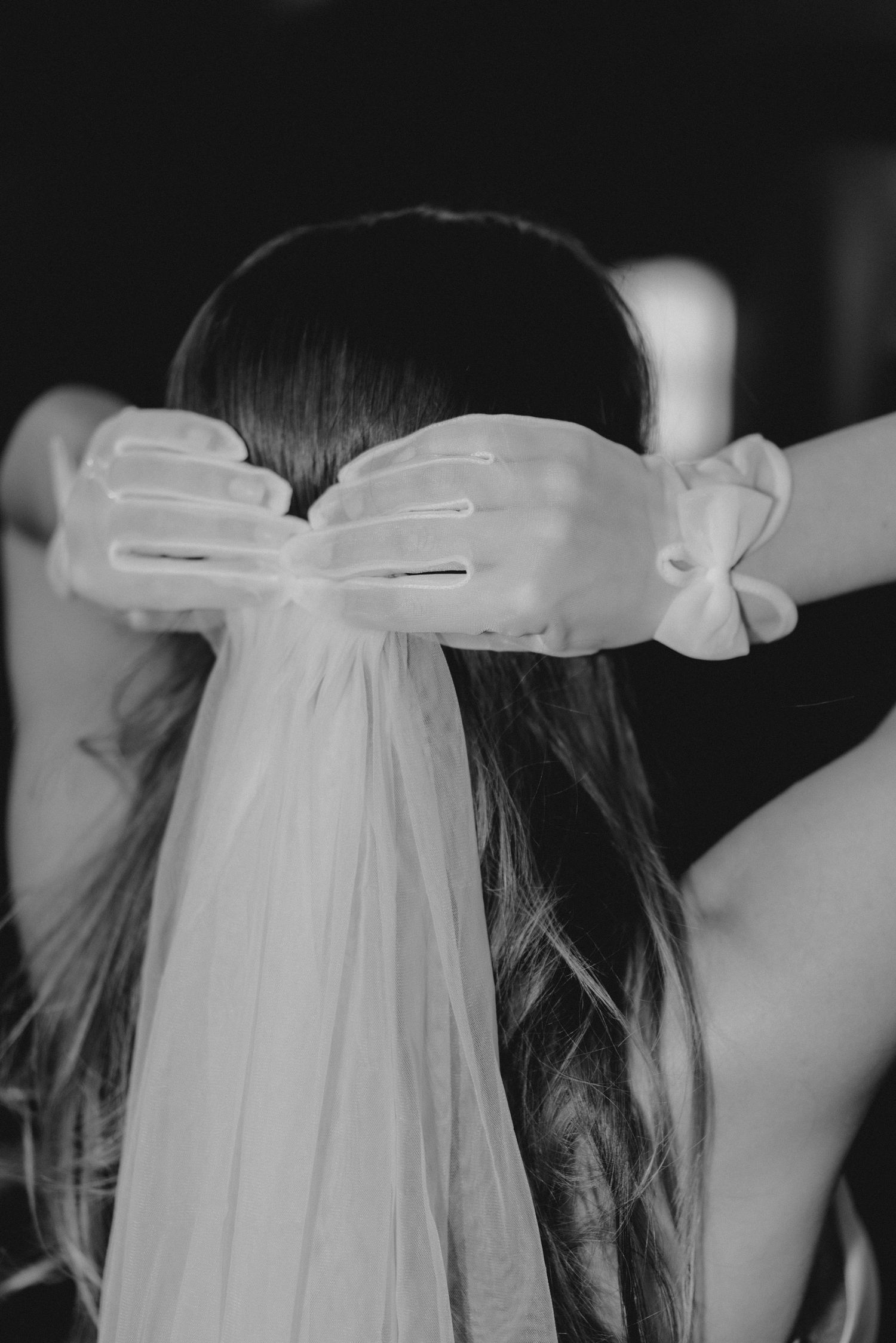 Close-up view of delicate white tulle veil with satin bow details against dark background.