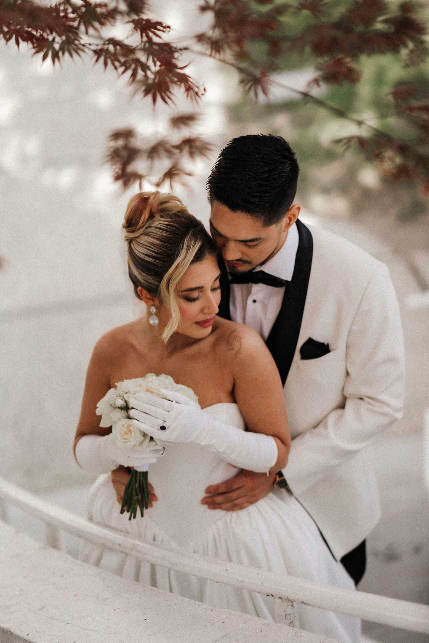 A tender wedding moment captured under red maple leaves outdoors.