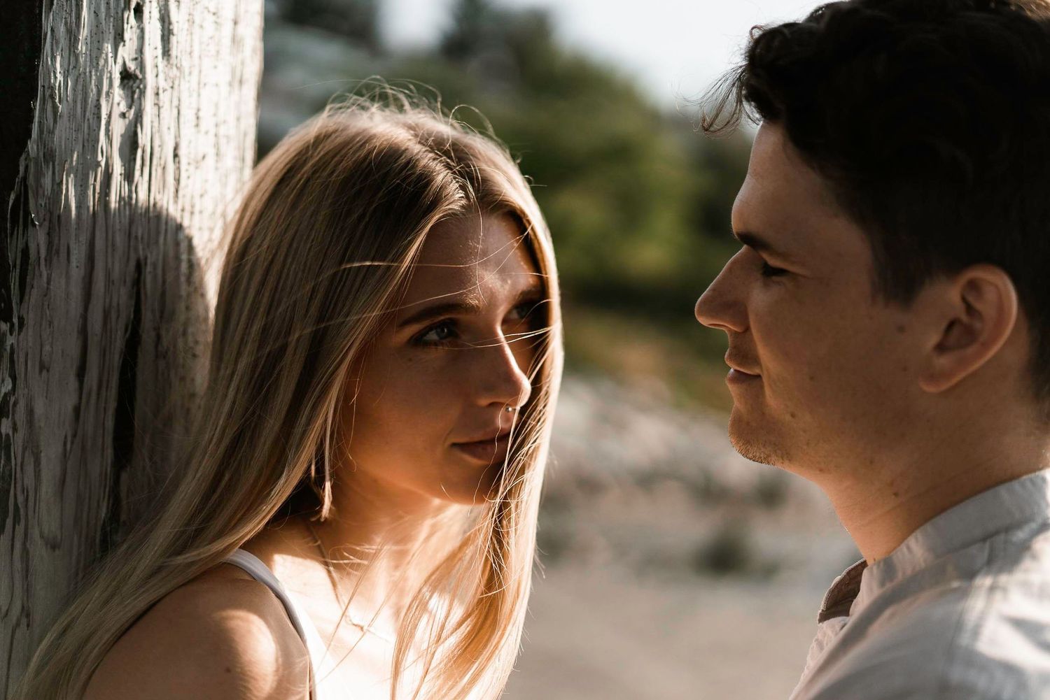 A couple stands close together in soft sunlight against a natural backdrop.