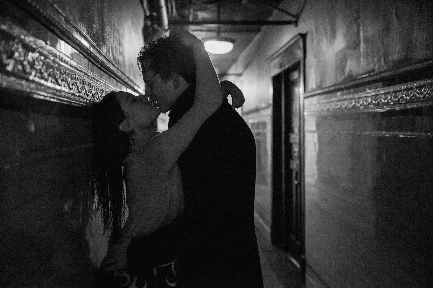 Film noir style romantic scene in dark hallway with dramatic lighting.