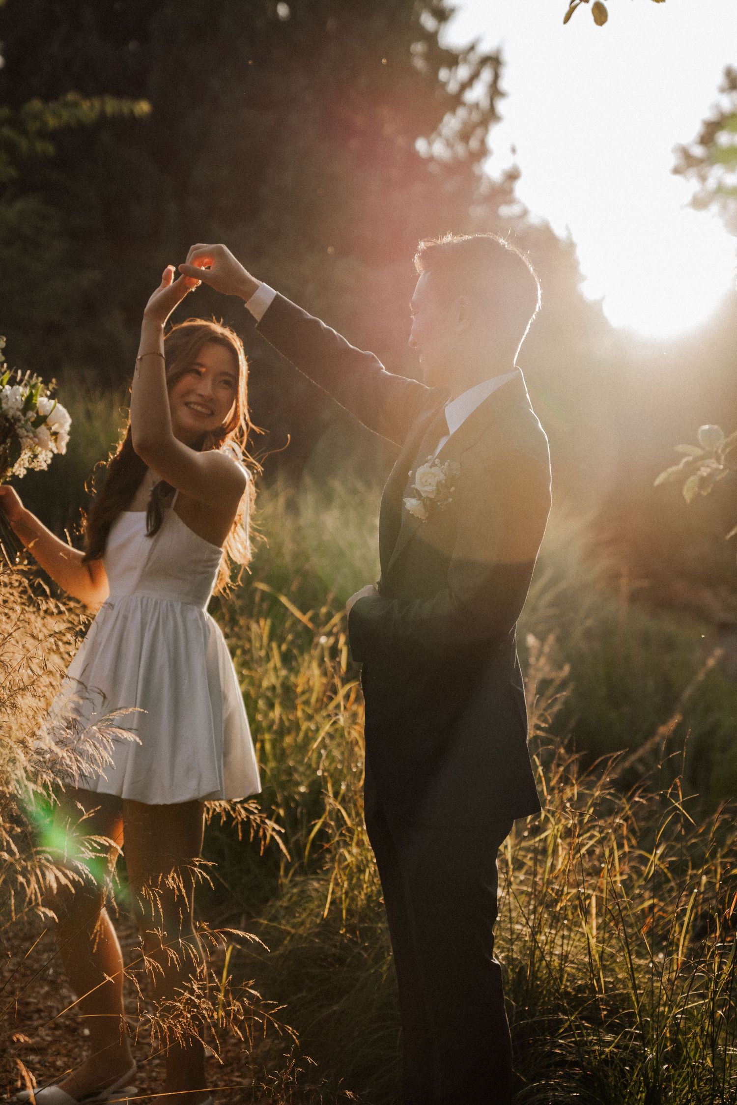 A couple dancing together in a sunlit field at golden hour, silhouetted against glowing summer evening light.