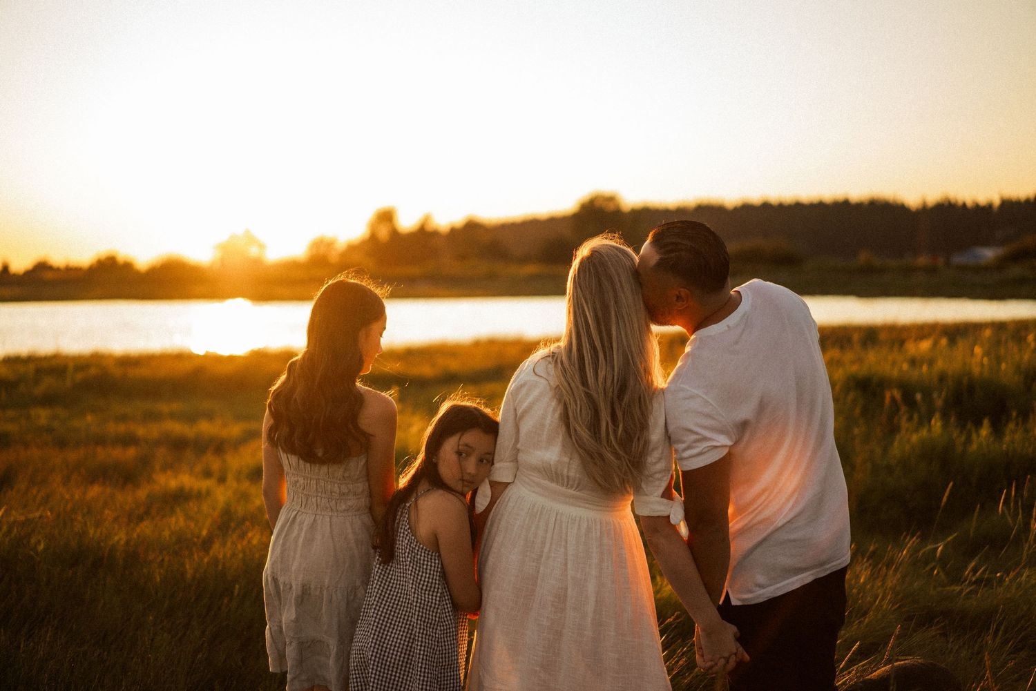 Silhouettes of family members against warm sunset sky near water.