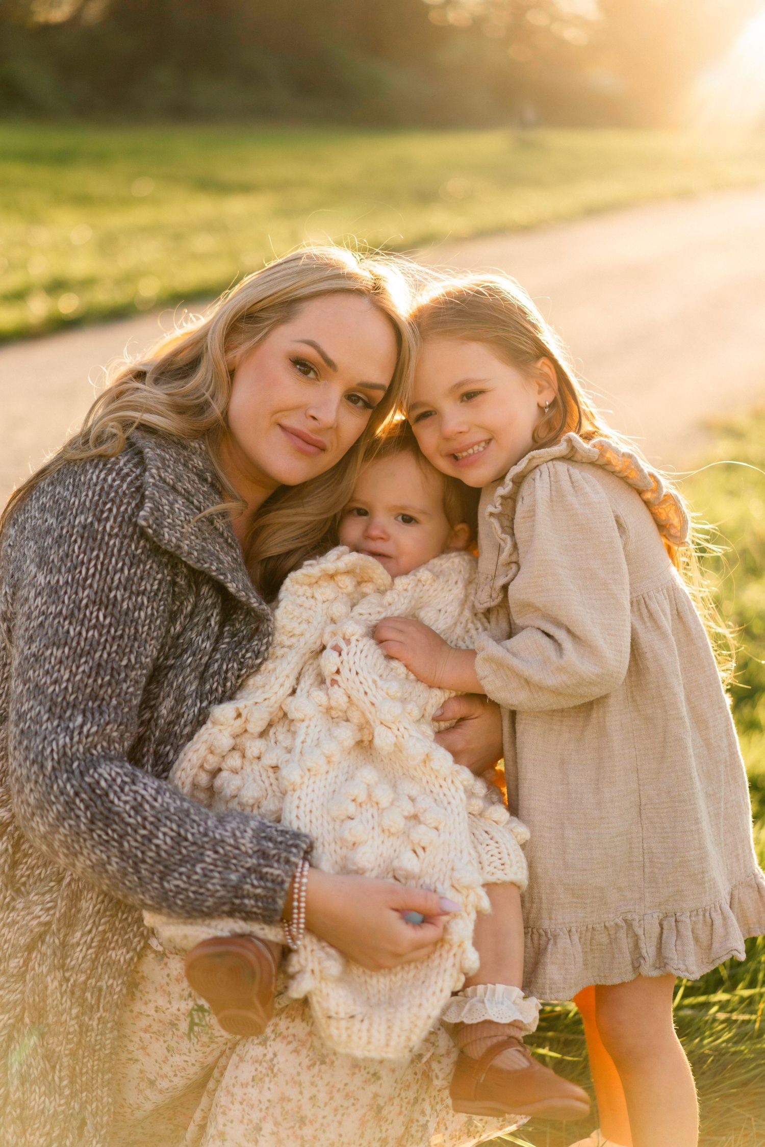 Family embracing in warm sunset light on grassy field.