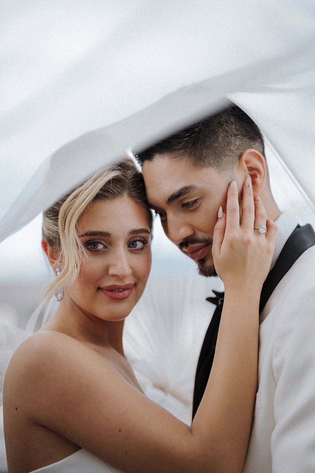 Intimate wedding portrait beneath a flowing white veil creating a romantic atmosphere.