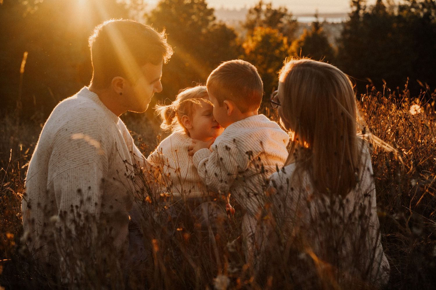 Silhouetted couple embracing in golden sunset light with sun flare peeking through trees.