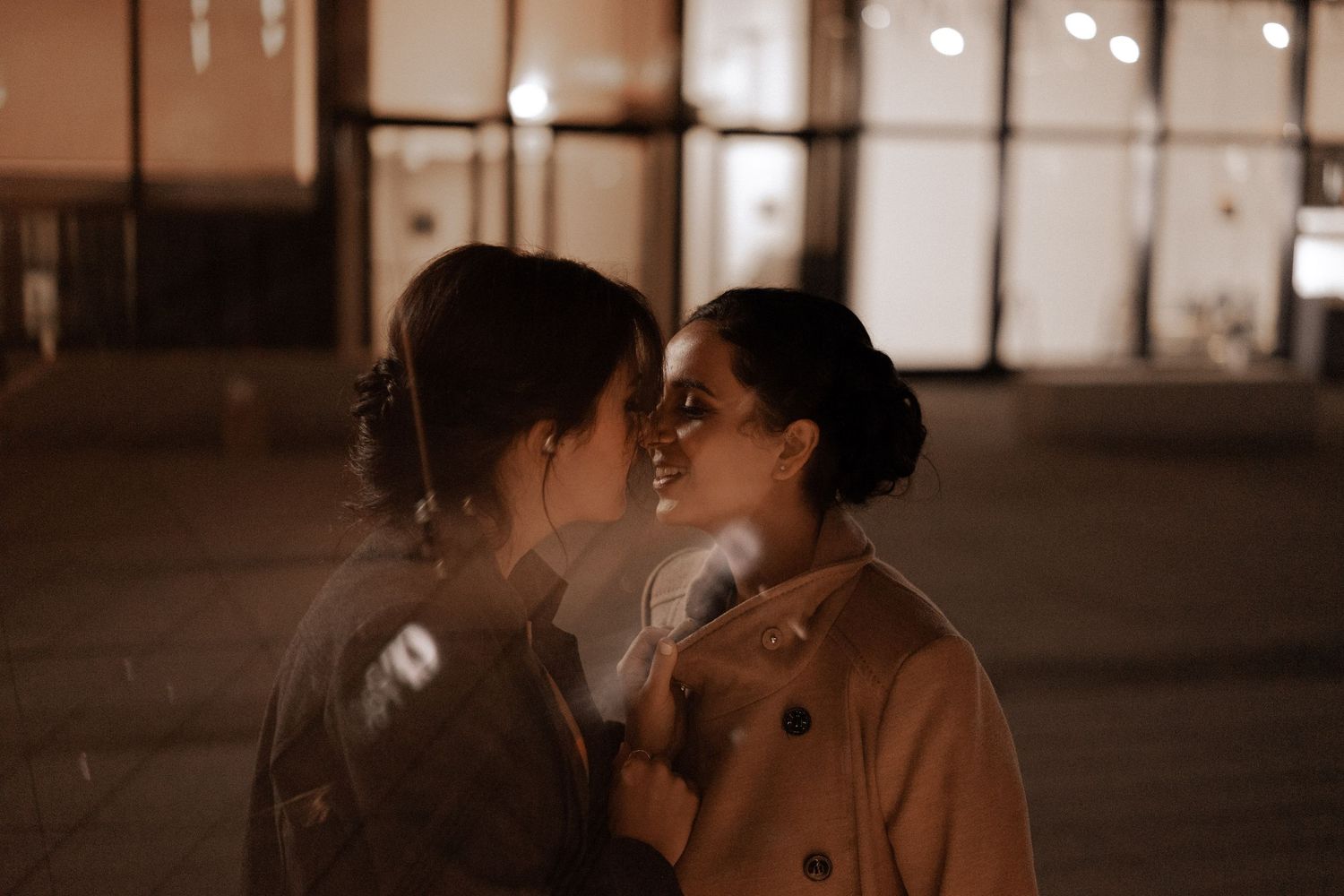 A romantic couple embraces in the shadows of a dimly lit room at night.