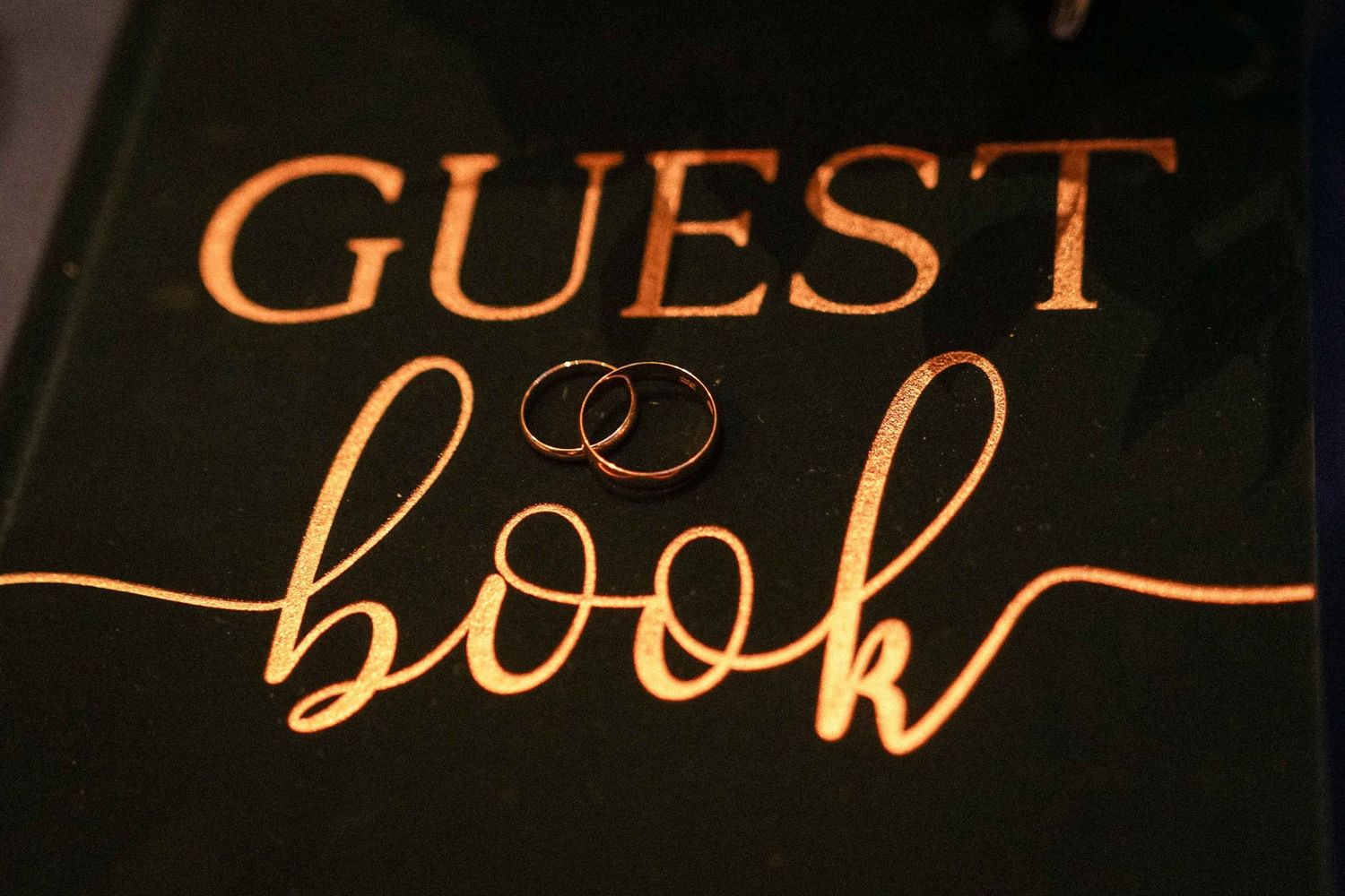 Illuminated guest sign with wedding rings displayed in golden lighting.