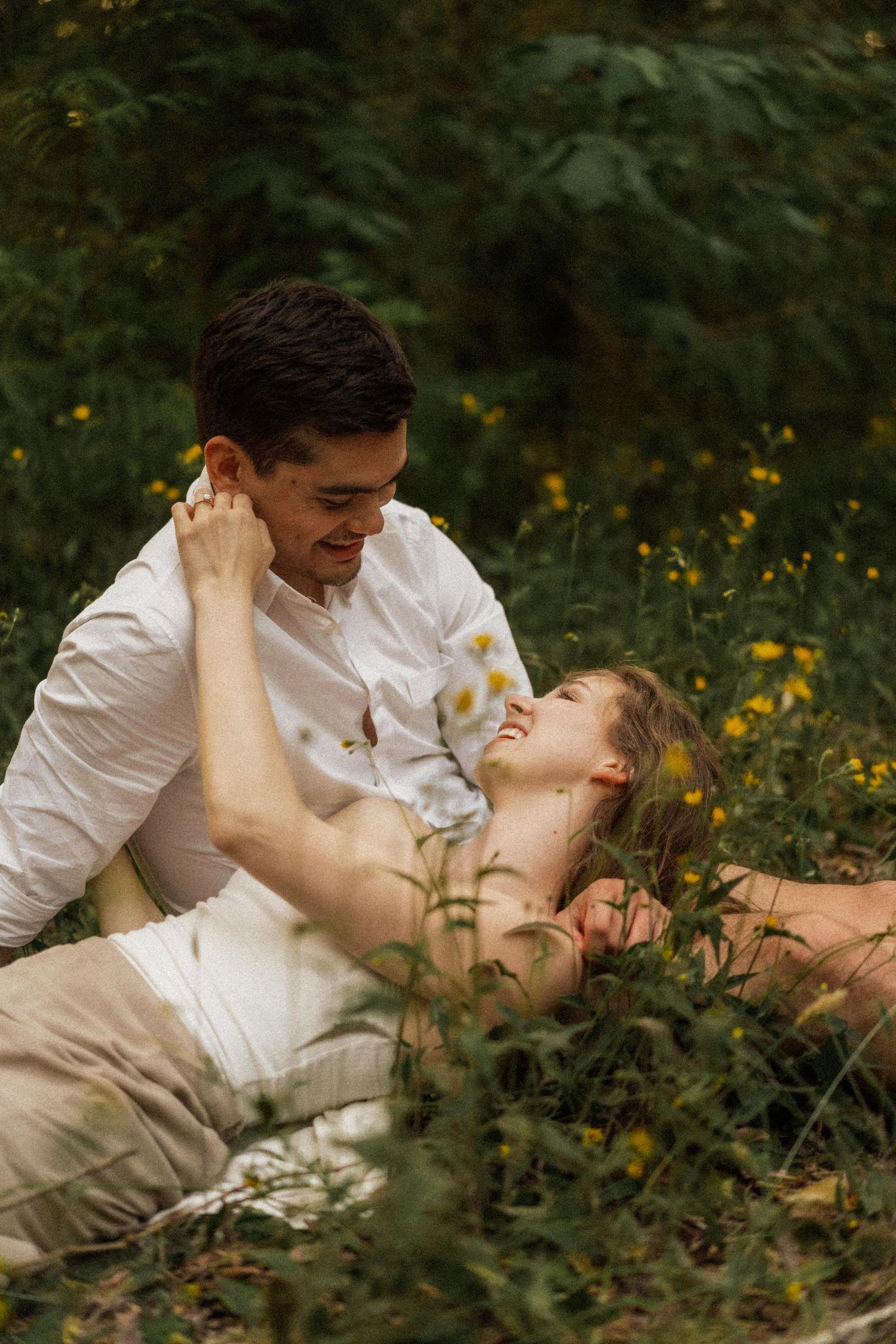 Romantic couple poses intimately among wildflowers in a forest setting.
