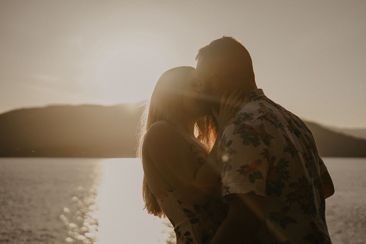 Silhouetted couple sharing intimate moment at sunset by waterfront.