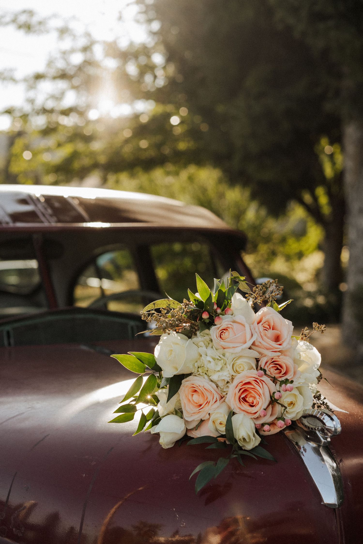 Peach and white roses decorating a vintage burgundy car at a wedding.