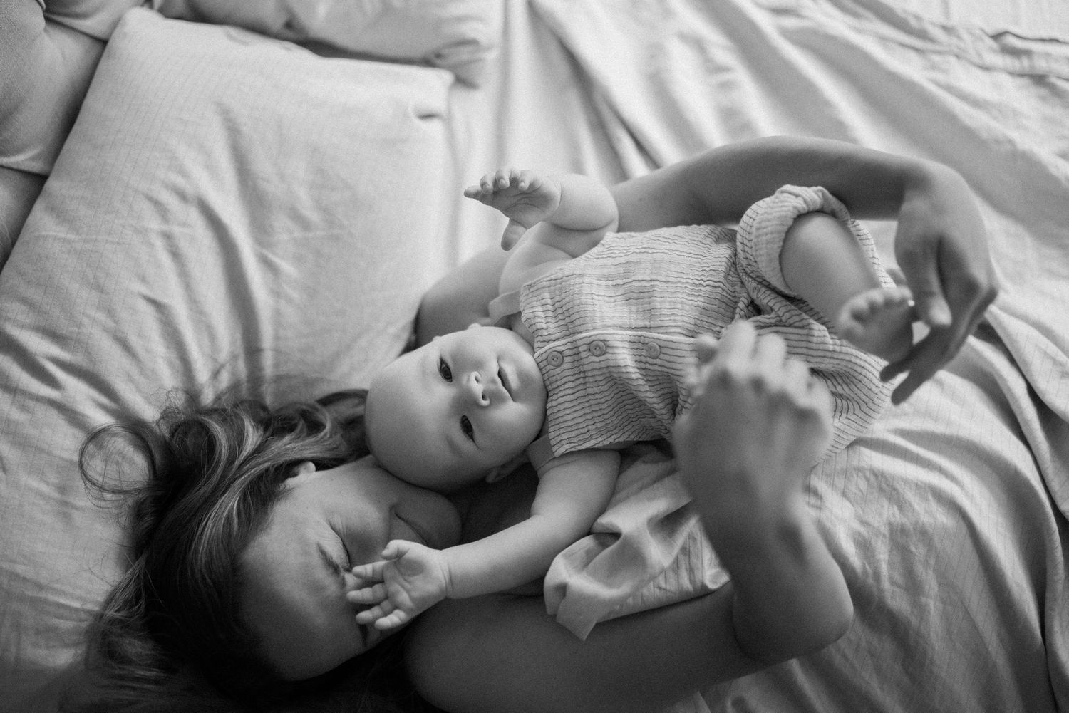 Intimate black and white photographs of tender family moments on white bedding.