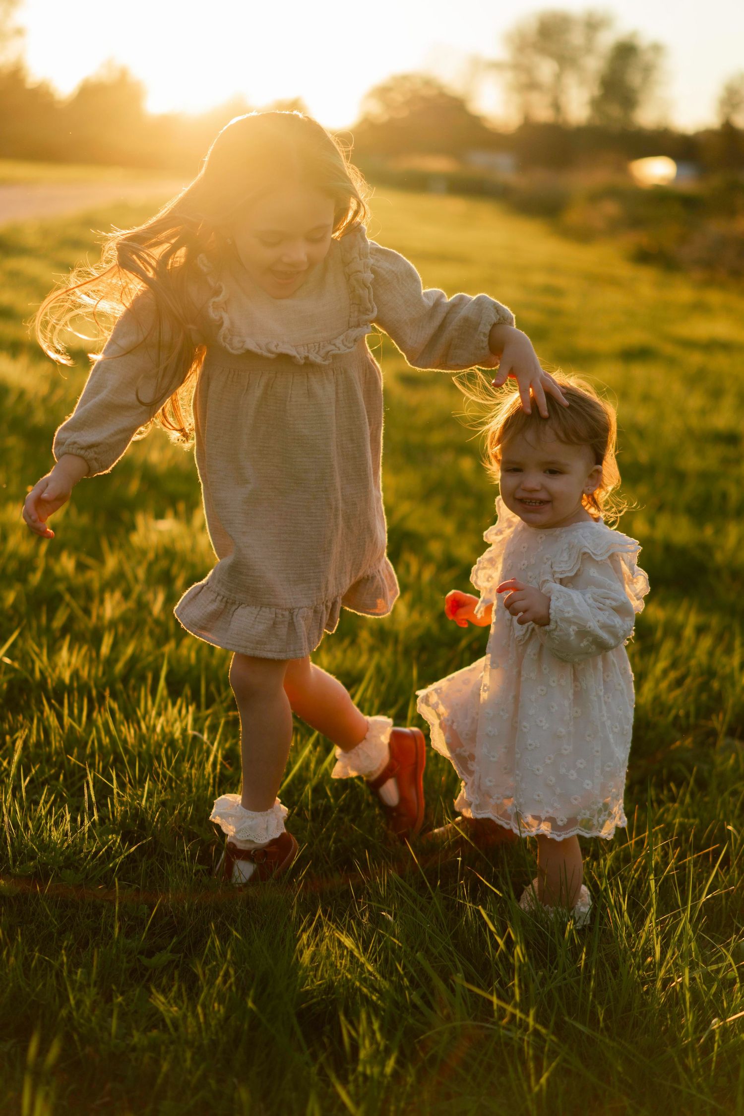 Child in flowing white dress runs through sunlit field at golden hour creating joyful movement.