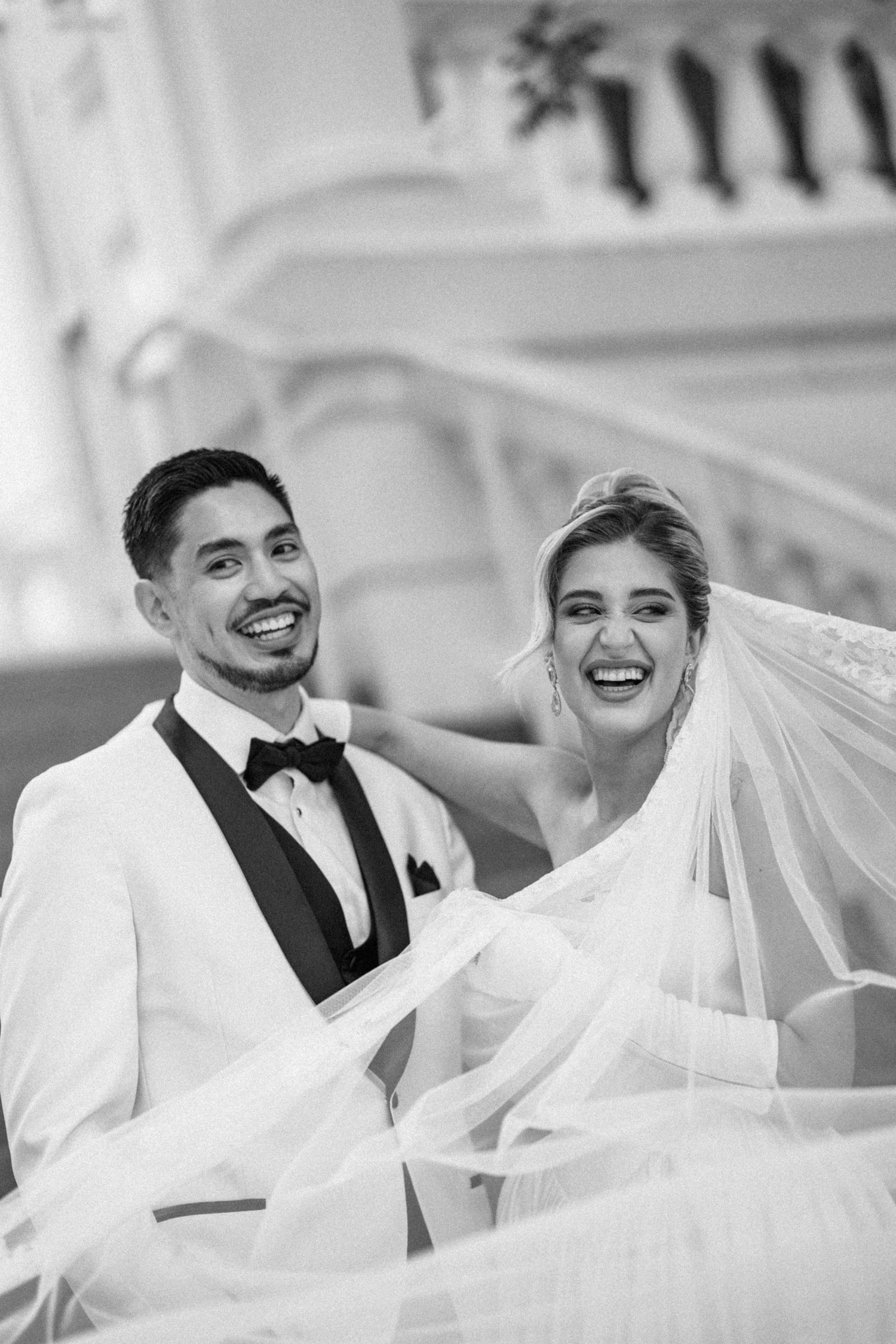 Joyful wedding couple sharing laughter under a flowing white veil.