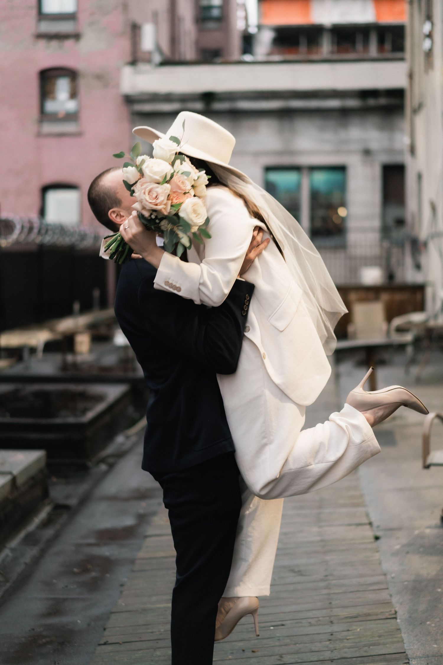 Playful couple in wedding attire dancing and twirling on an urban rooftop.