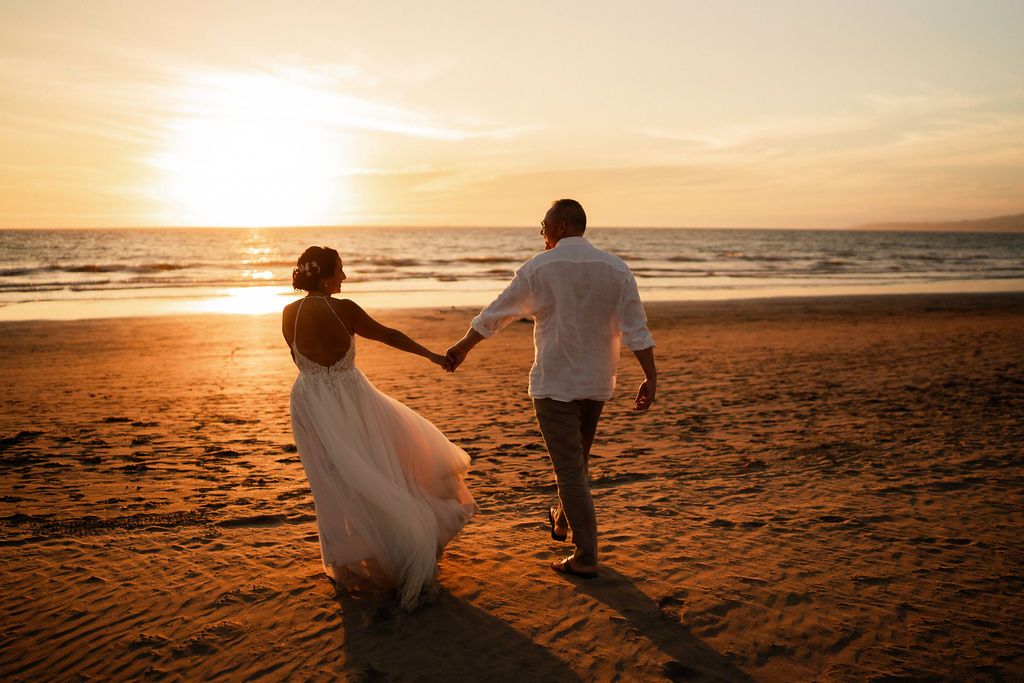 Silhouettes of a couple walking on the beach at sunset holding hands.