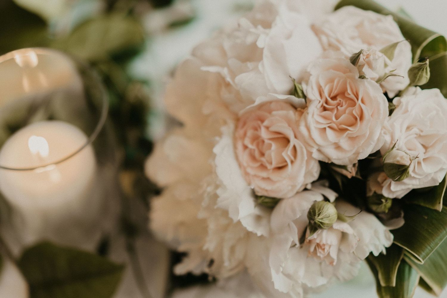 Delicate blush pink carnations and roses arranged with glowing candlelight create a romantic wedding centerpiece.