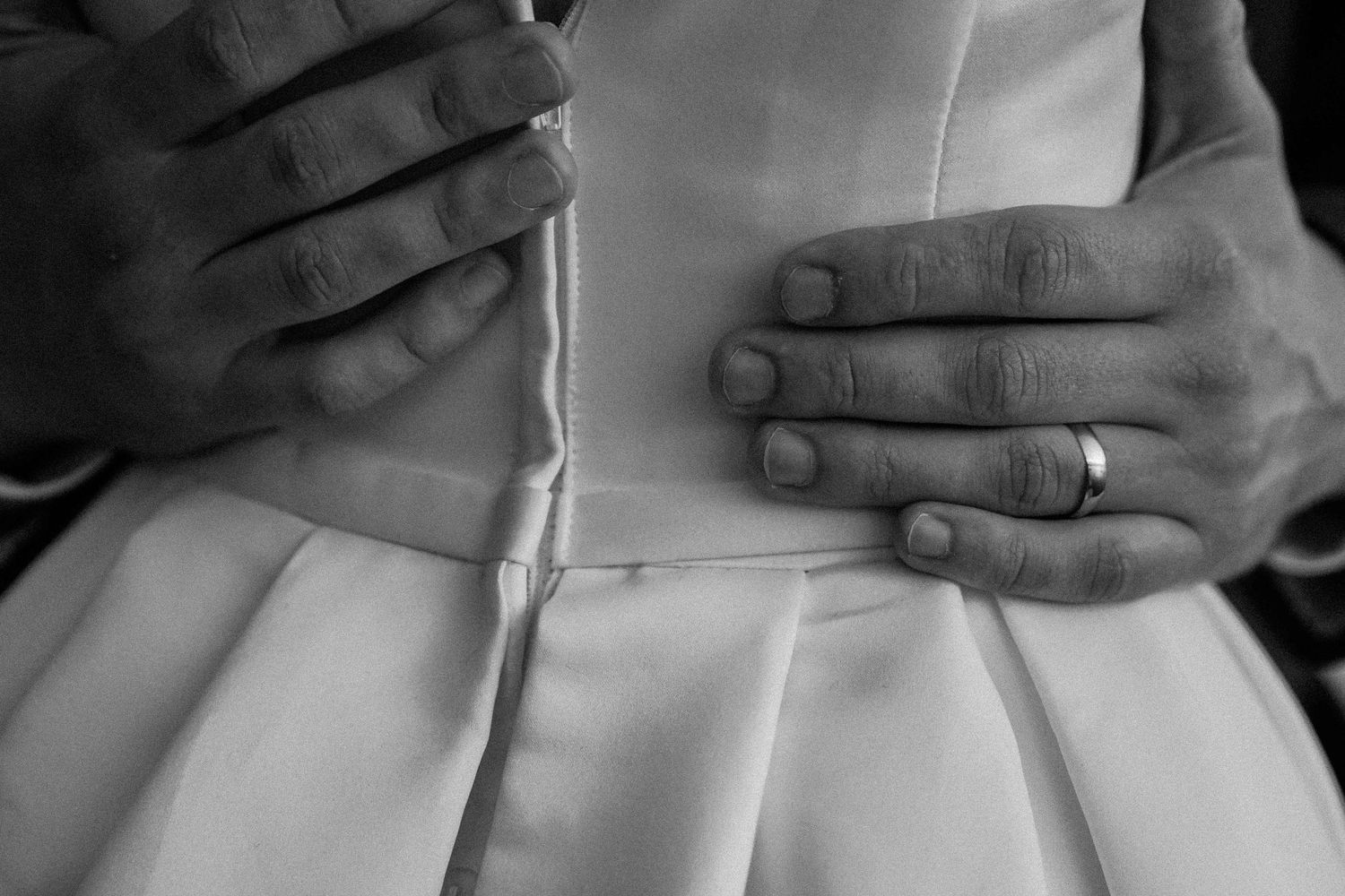 Detail shot of hands adjusting white formal dress pleats in black and white.