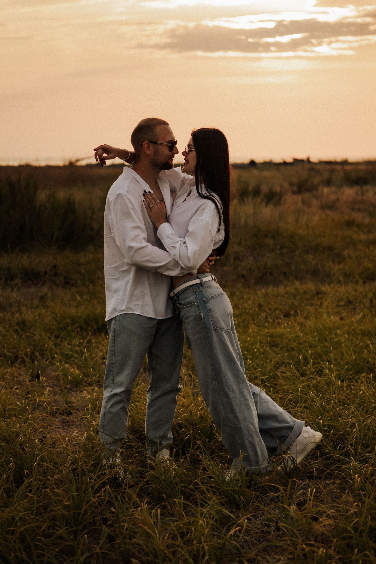 A romantic couple embraces in a golden-lit field at sunset creating a series of intimate silhouettes.