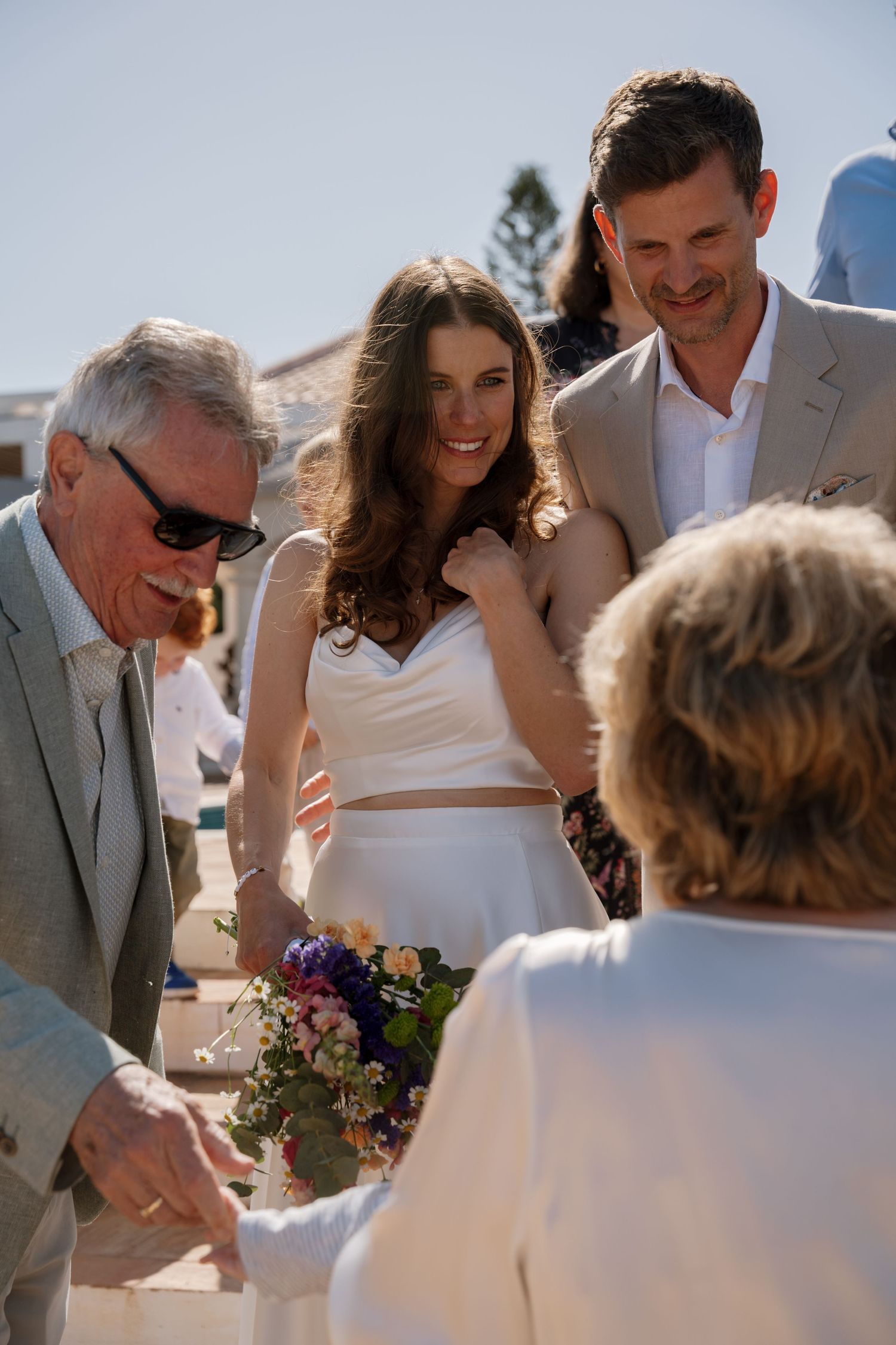 Bride and groom greet elderly guests while holding colorful wedding bouquet.