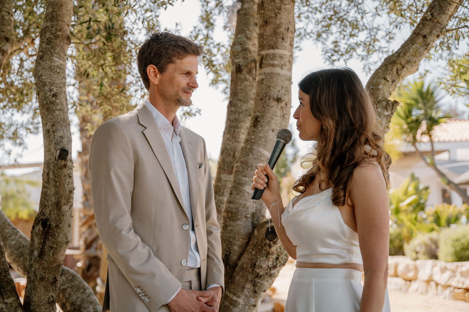 Bride speaks into a microphone while facing her groom during an intimate outdoor wedding ceremony.
