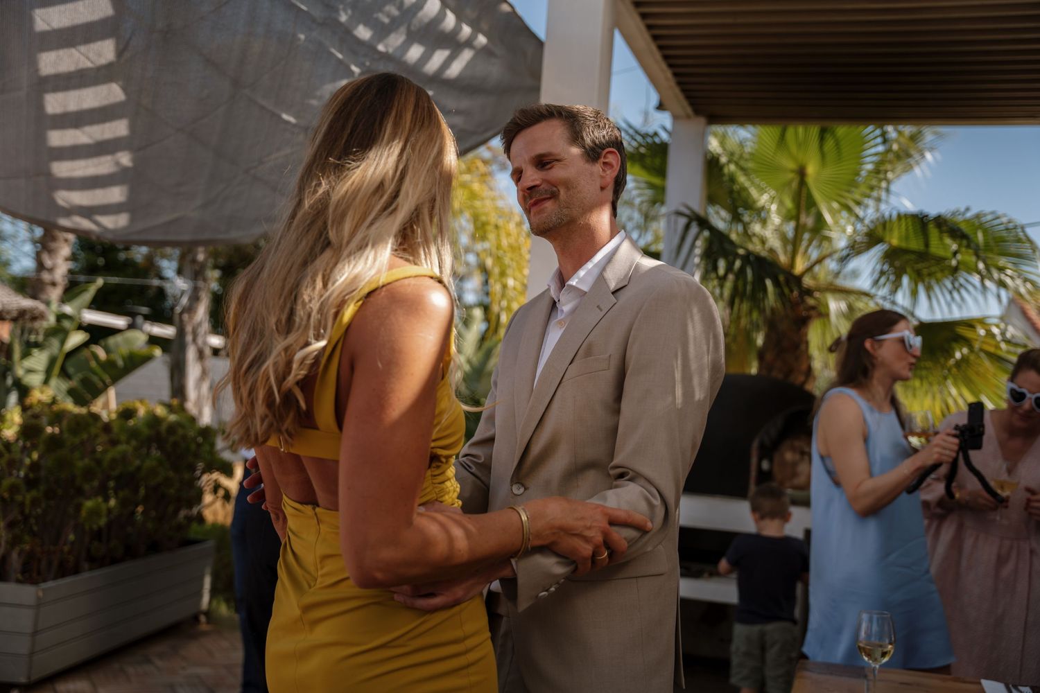 Man in beige suit dances with woman in yellow dress at outdoor reception.