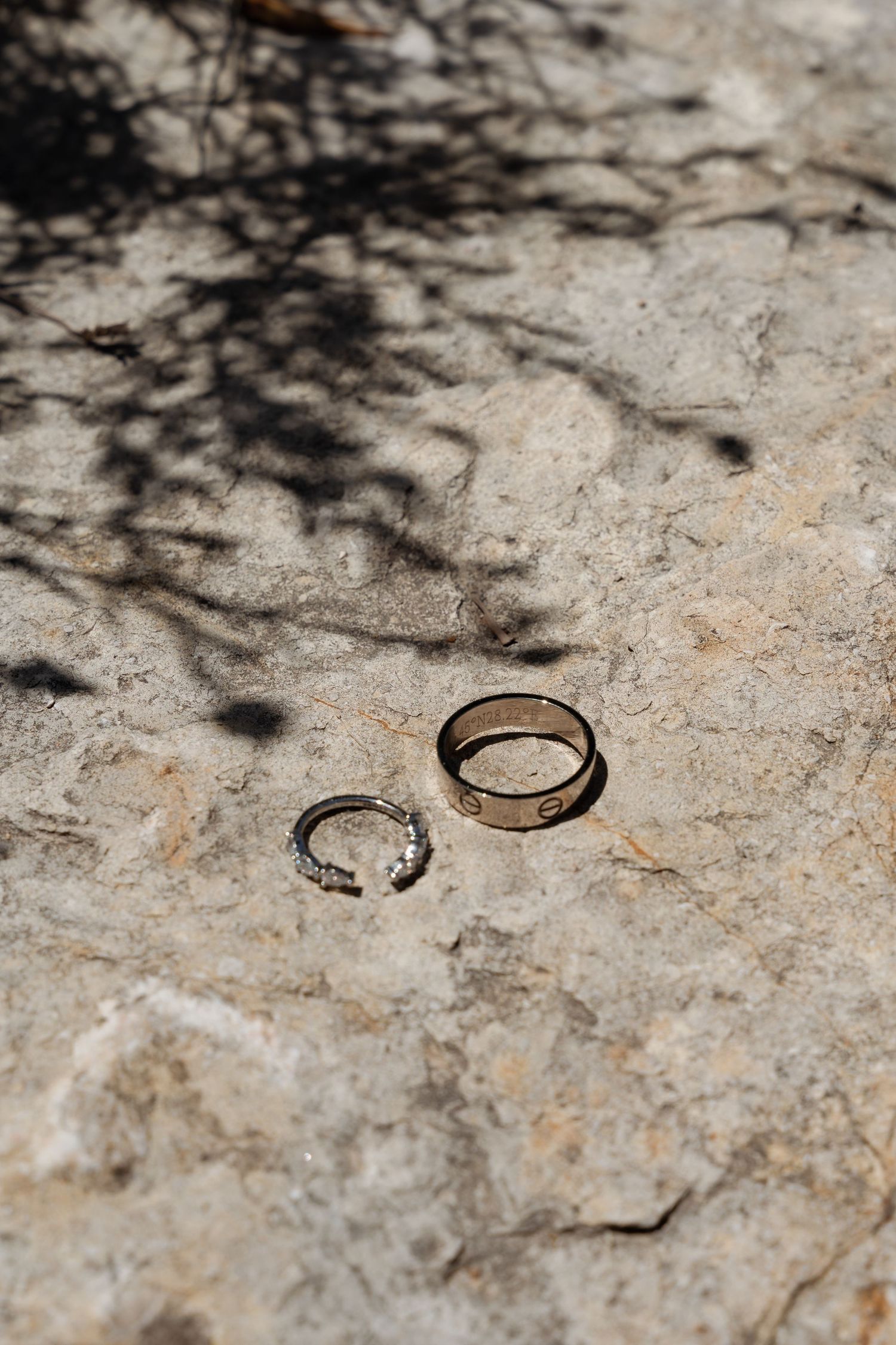 Two wedding rings, a diamond band and gold band, rest on a sunlit stone surface.