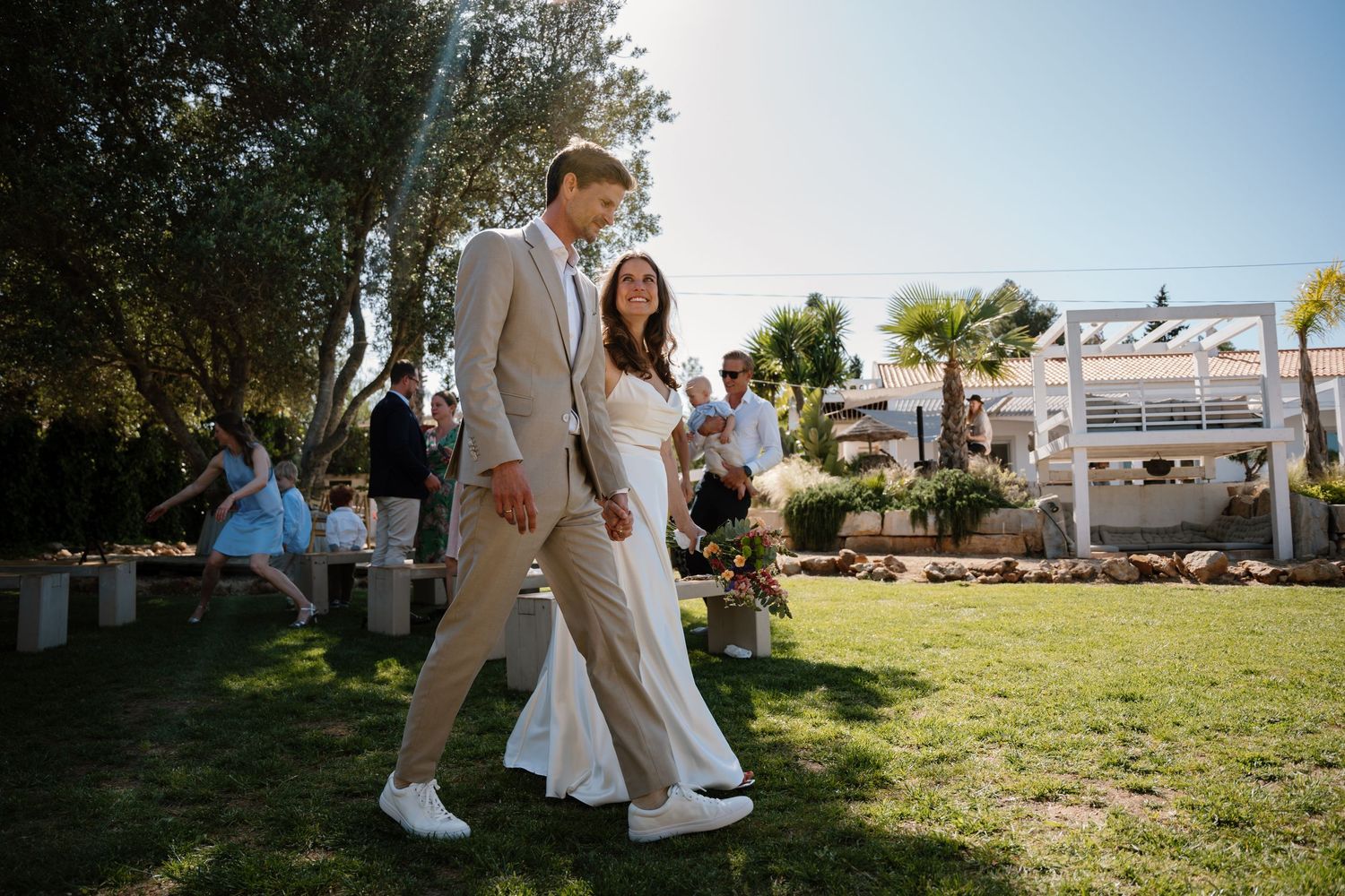 Newlyweds walk hand in hand through garden after outdoor wedding ceremony.