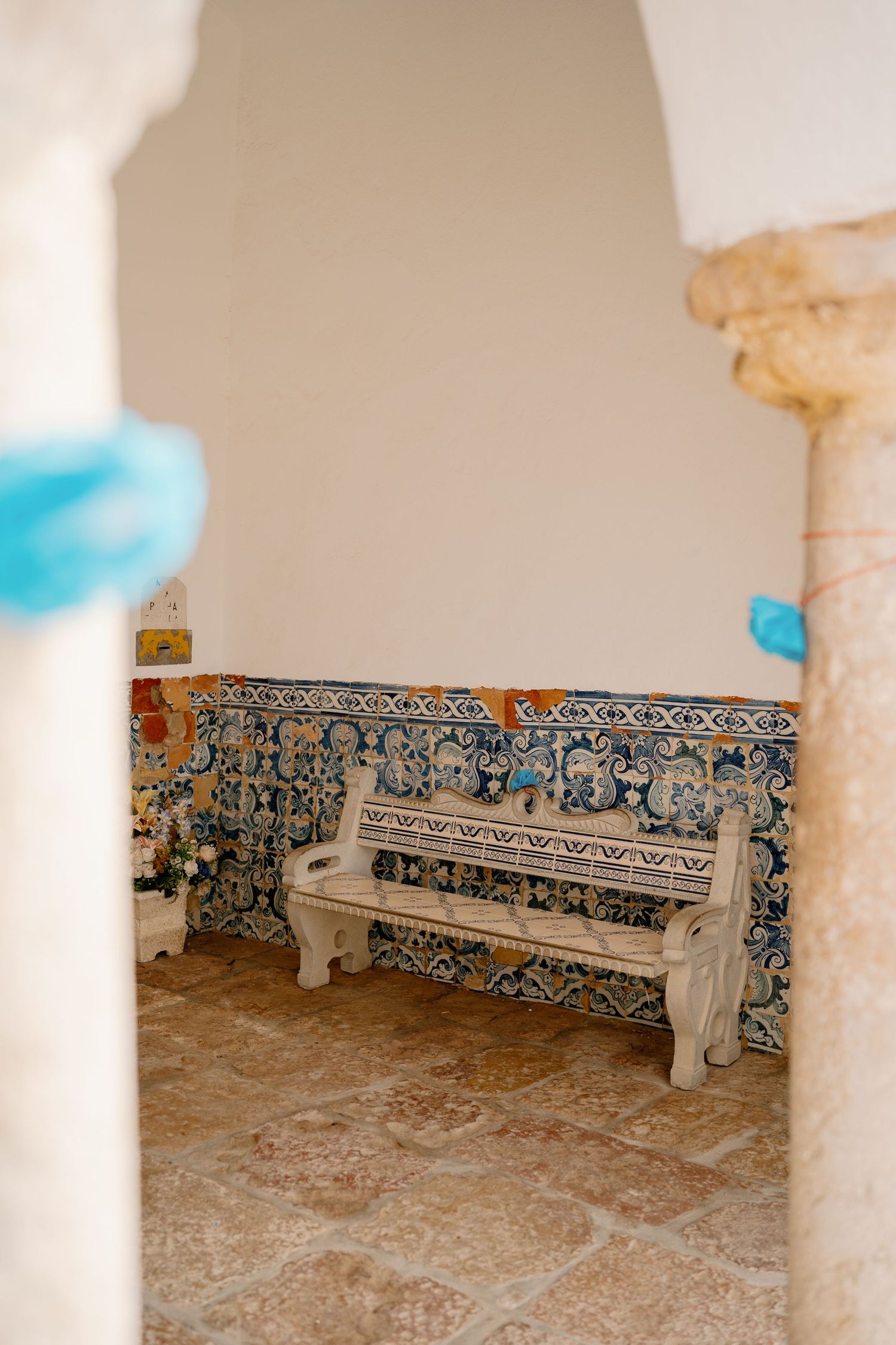 Vintage stone bench against ornate blue and white azulejo tile wall in a Portuguese courtyard alcove.
