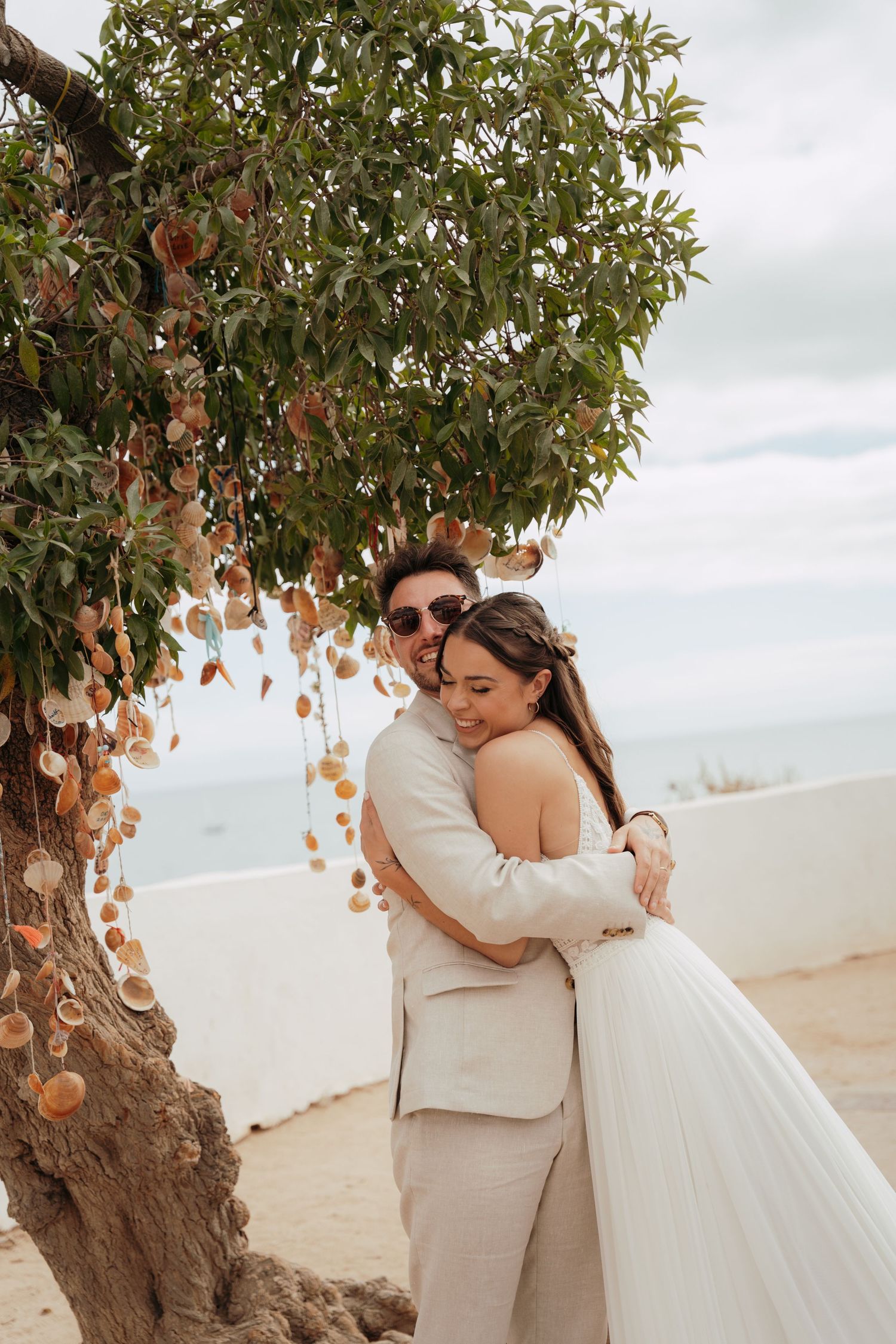 Bride and groom embracing under a fruit tree with ocean views on their wedding day.