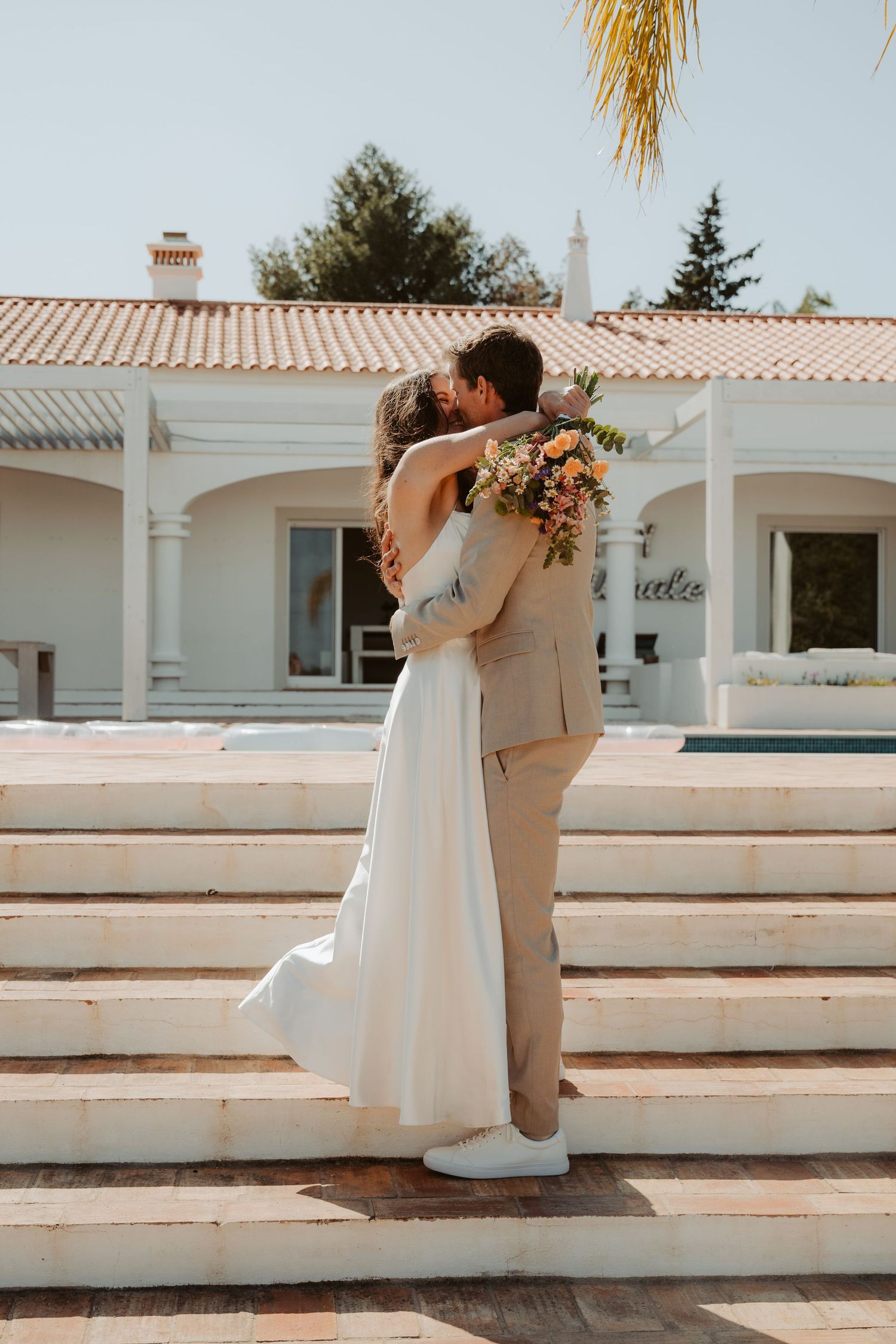 Bride and groom sharing a kiss on white steps outside a Mediterranean villa.