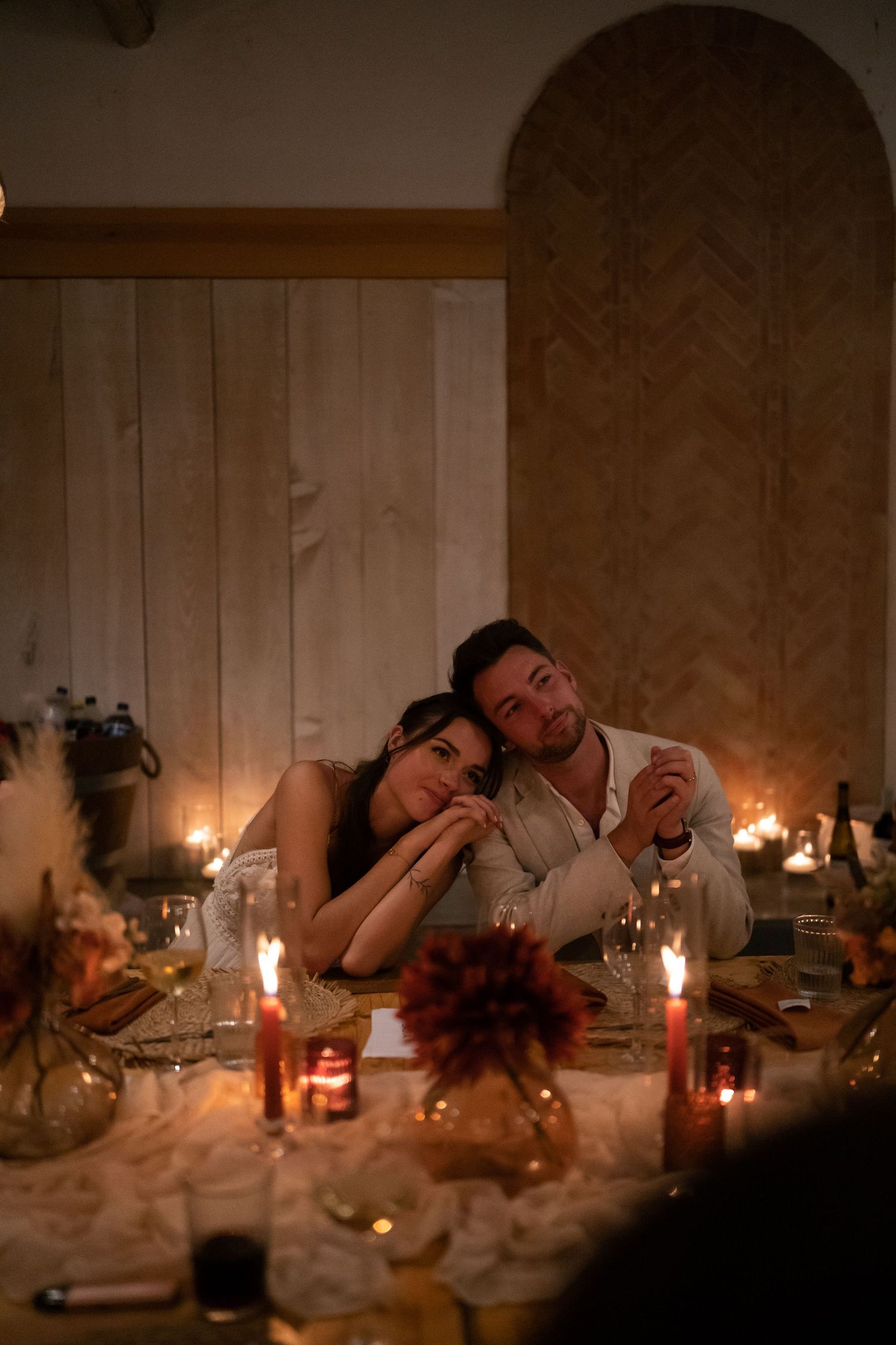 Couple sharing a romantic candlelit dinner, leaning together at a beautifully decorated table with warm glowing candles.
