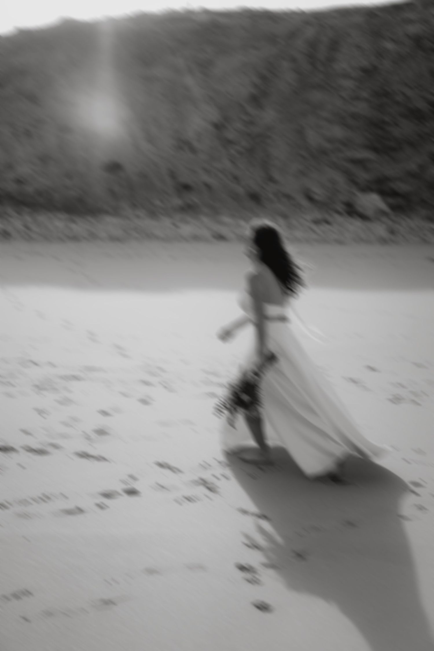 Black and white motion blur photo of bride running along sandy beach at sunset.