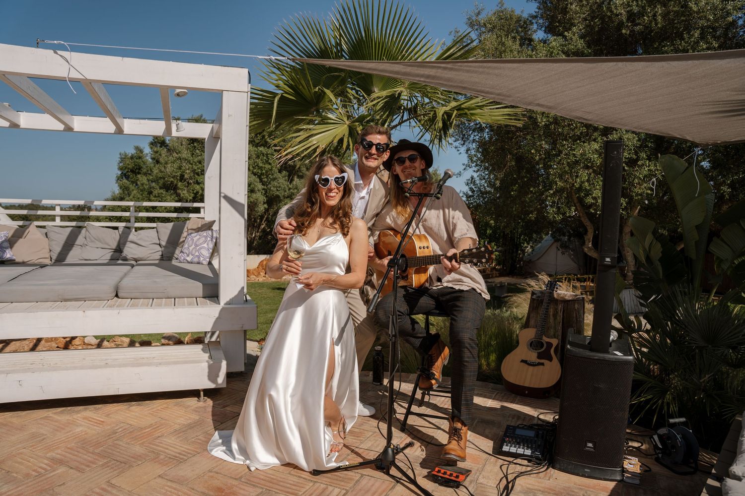Bride and groom posing with guitarist musician at outdoor wedding garden celebration.