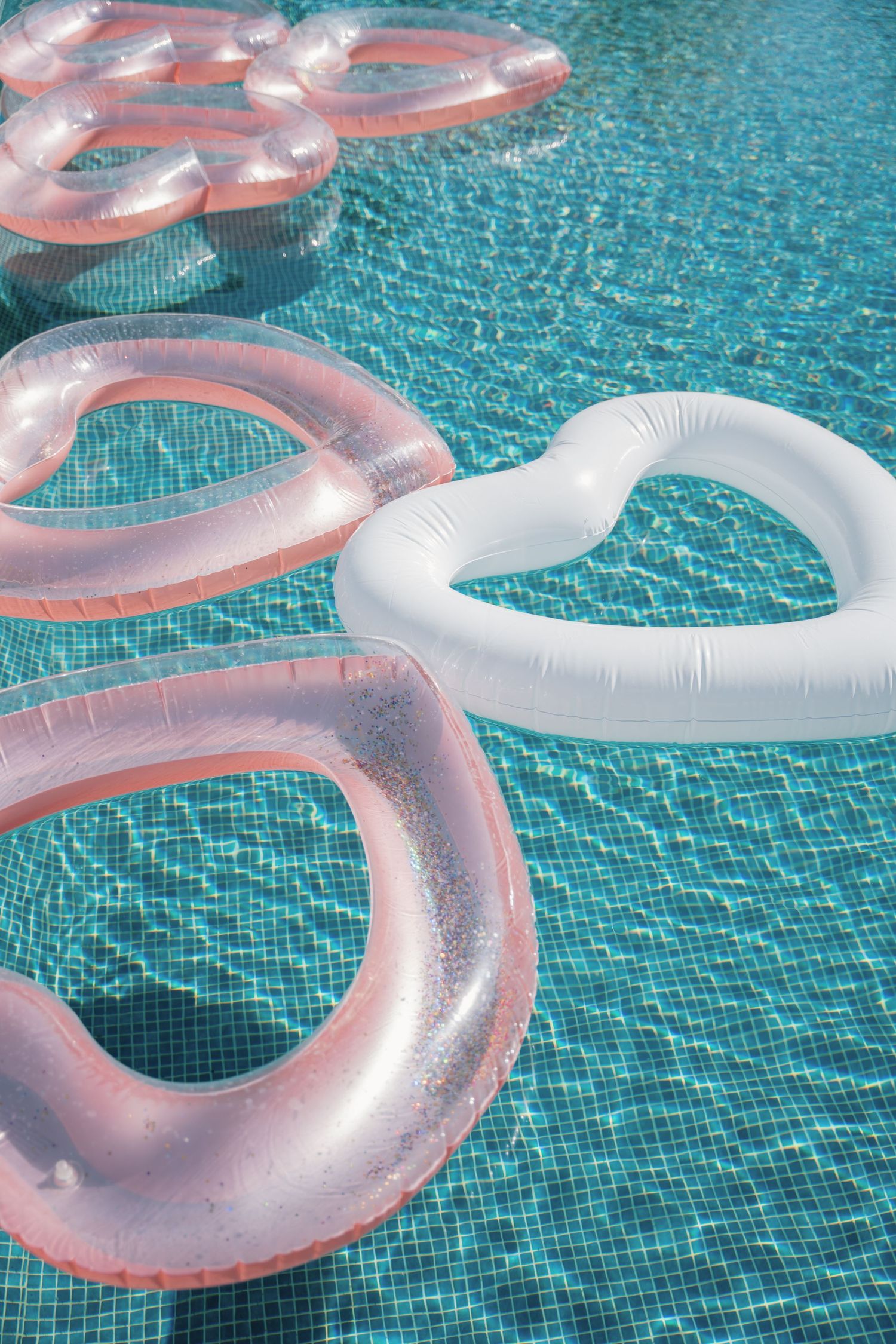 Pink and white heart-shaped inflatable pool floats floating in a bright turquoise swimming pool.