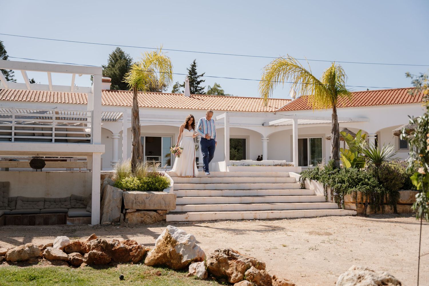 Bride and groom walking down steps outside a white Mediterranean wedding venue.