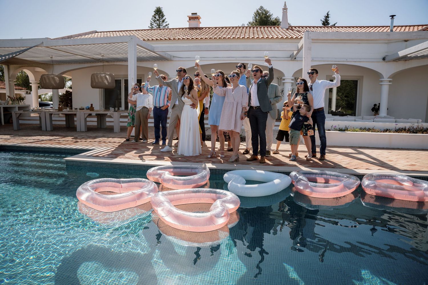 Wedding party group photo beside pool with heart-shaped pink and white inflatable floats.