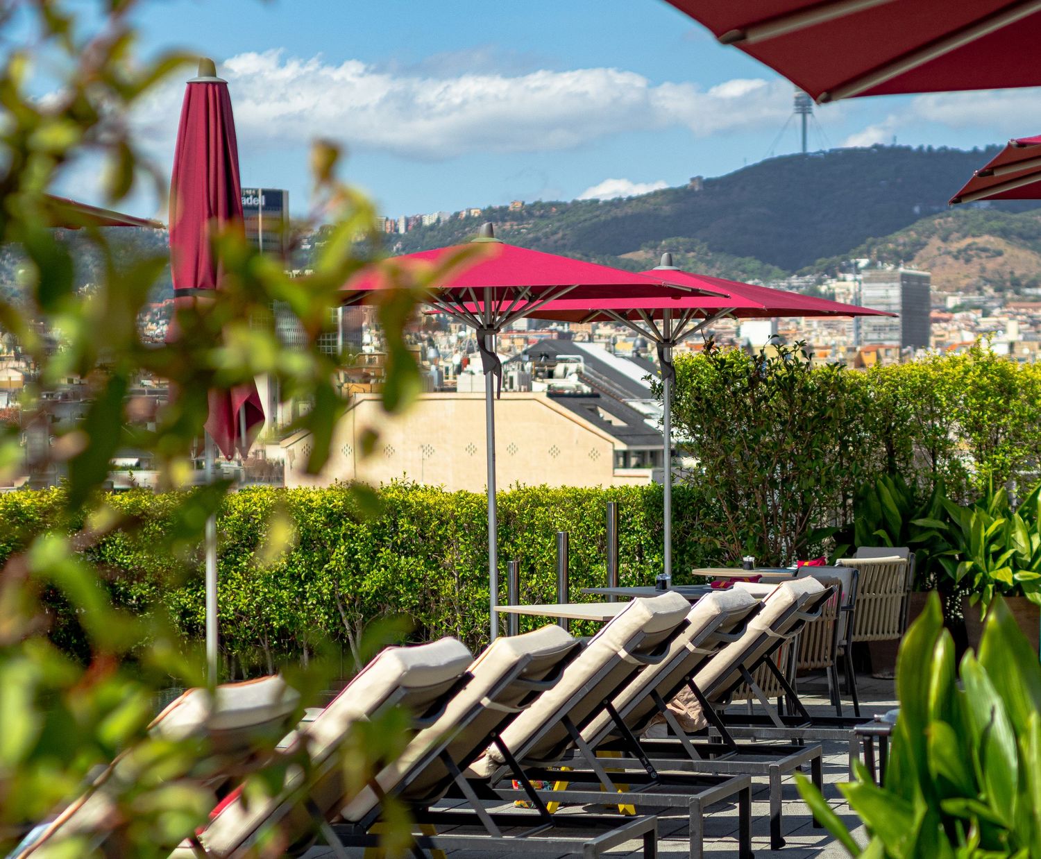 Rooftop terrace with red umbrellas, lounge chairs, and panoramic city and mountain views. hotel photographe montpellier france