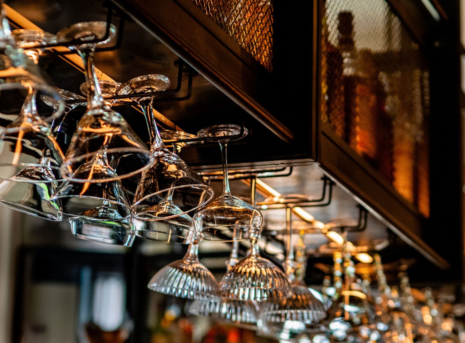 Crystal wine glasses stored upside down on a bar rack with golden bokeh background lighting.