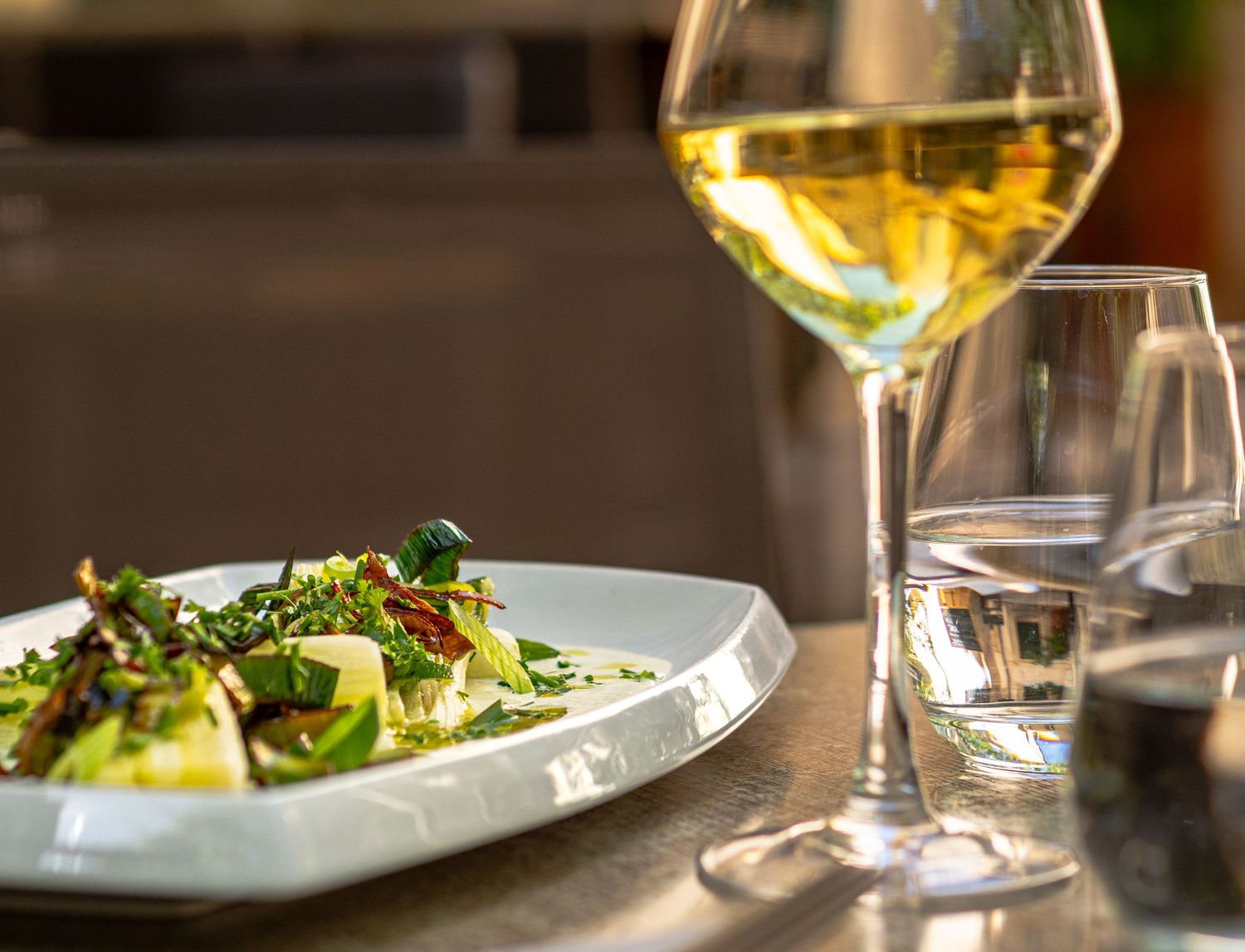 A gourmet salad plate with fresh greens beside a glass of white wine and water glass on a restaurant table. Montpellier photographe