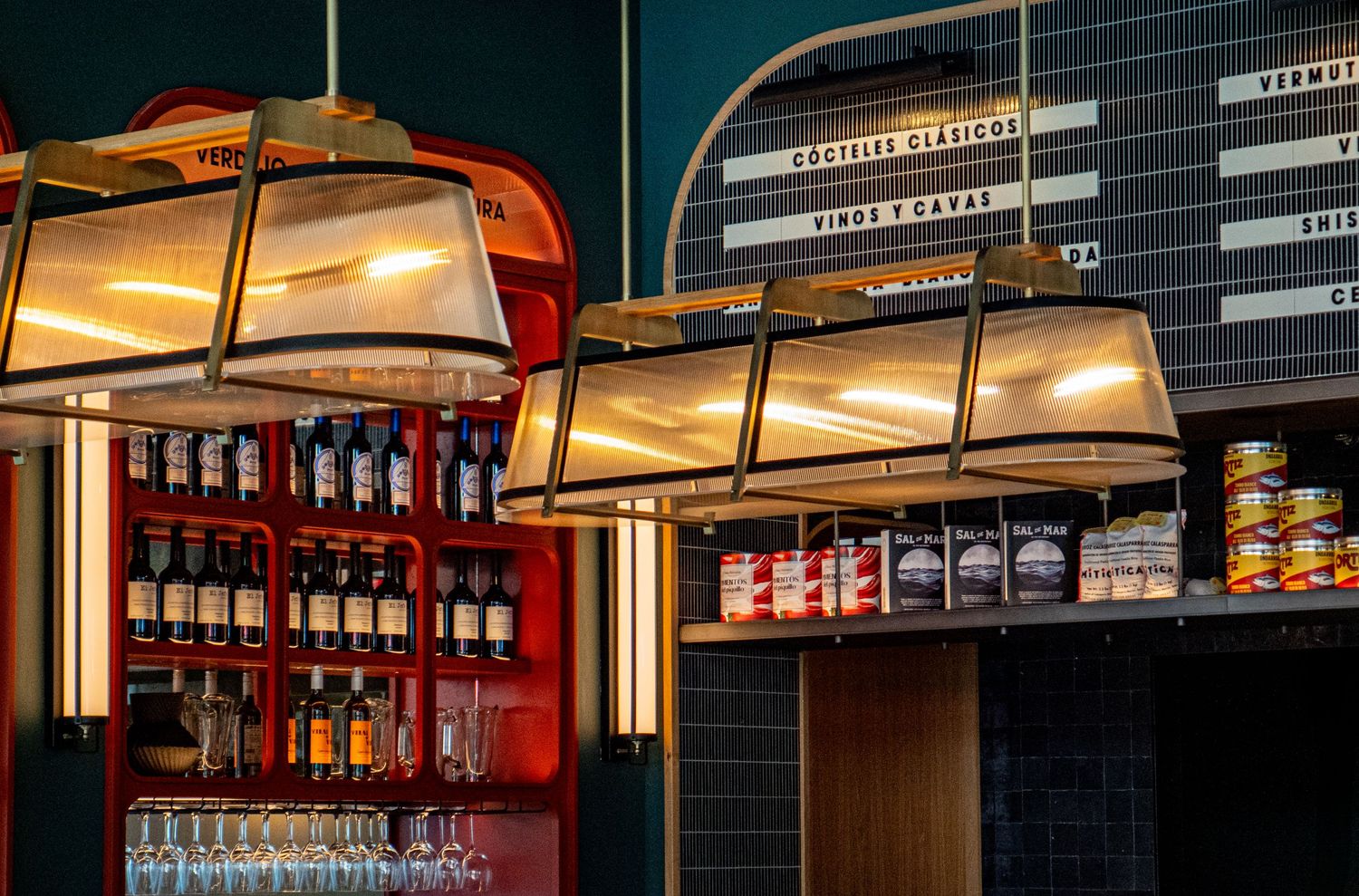 Stylish bar interior with pendant lights, shelved spirits, and a menu board displaying cocktails and wines.