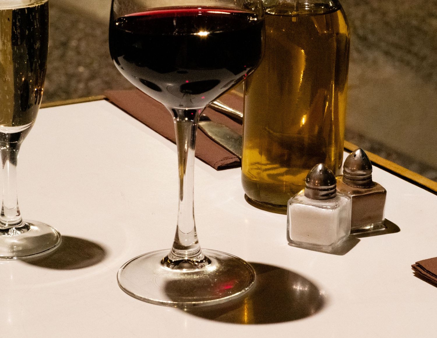 Red wine in elegant glass beside olive oil bottle, salt and pepper shakers on white table. French restaurant photography