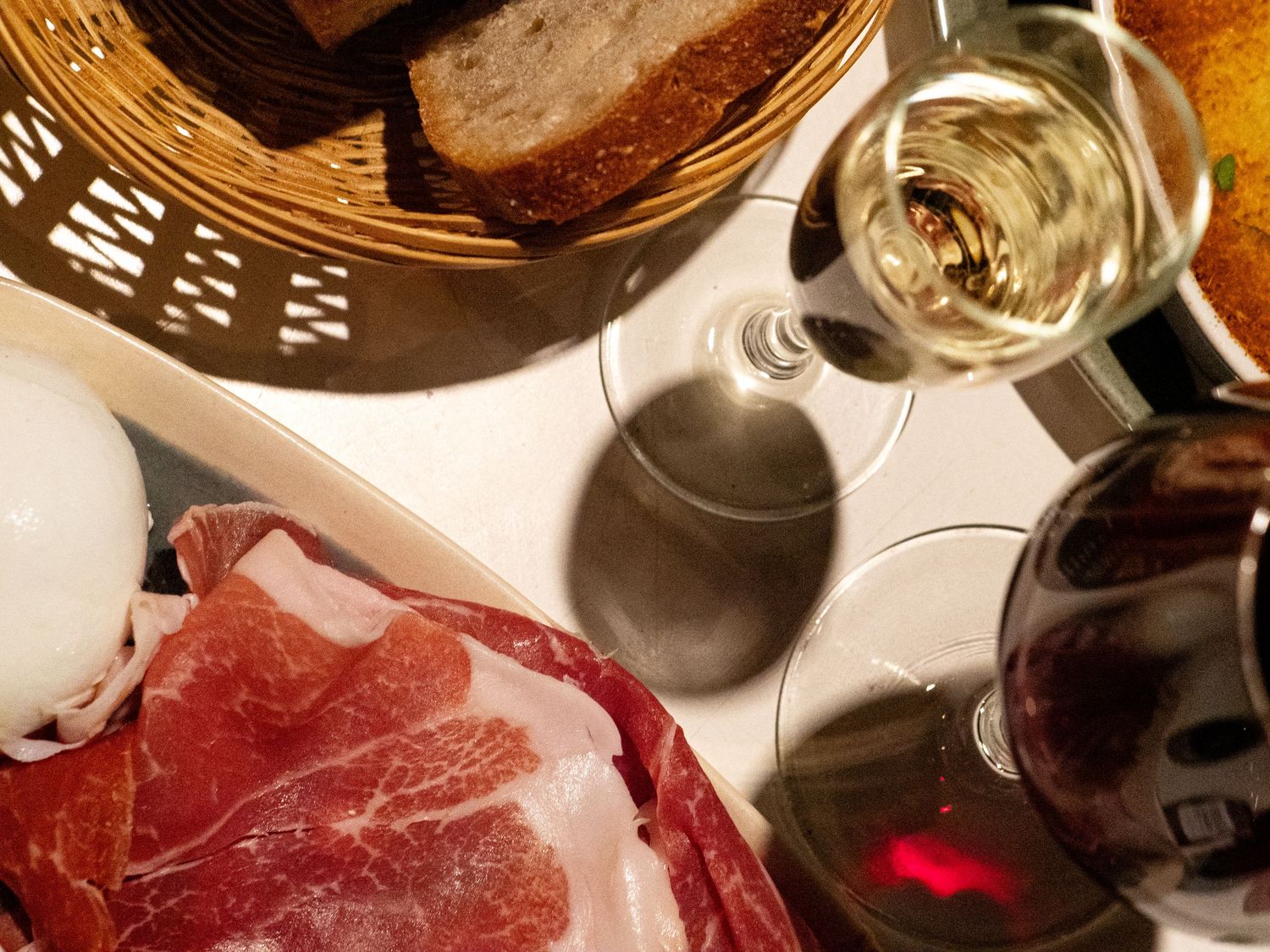 Charcuterie board with prosciutto, bread basket, white and red wine glasses on a white tablecloth. France restaurant photographe