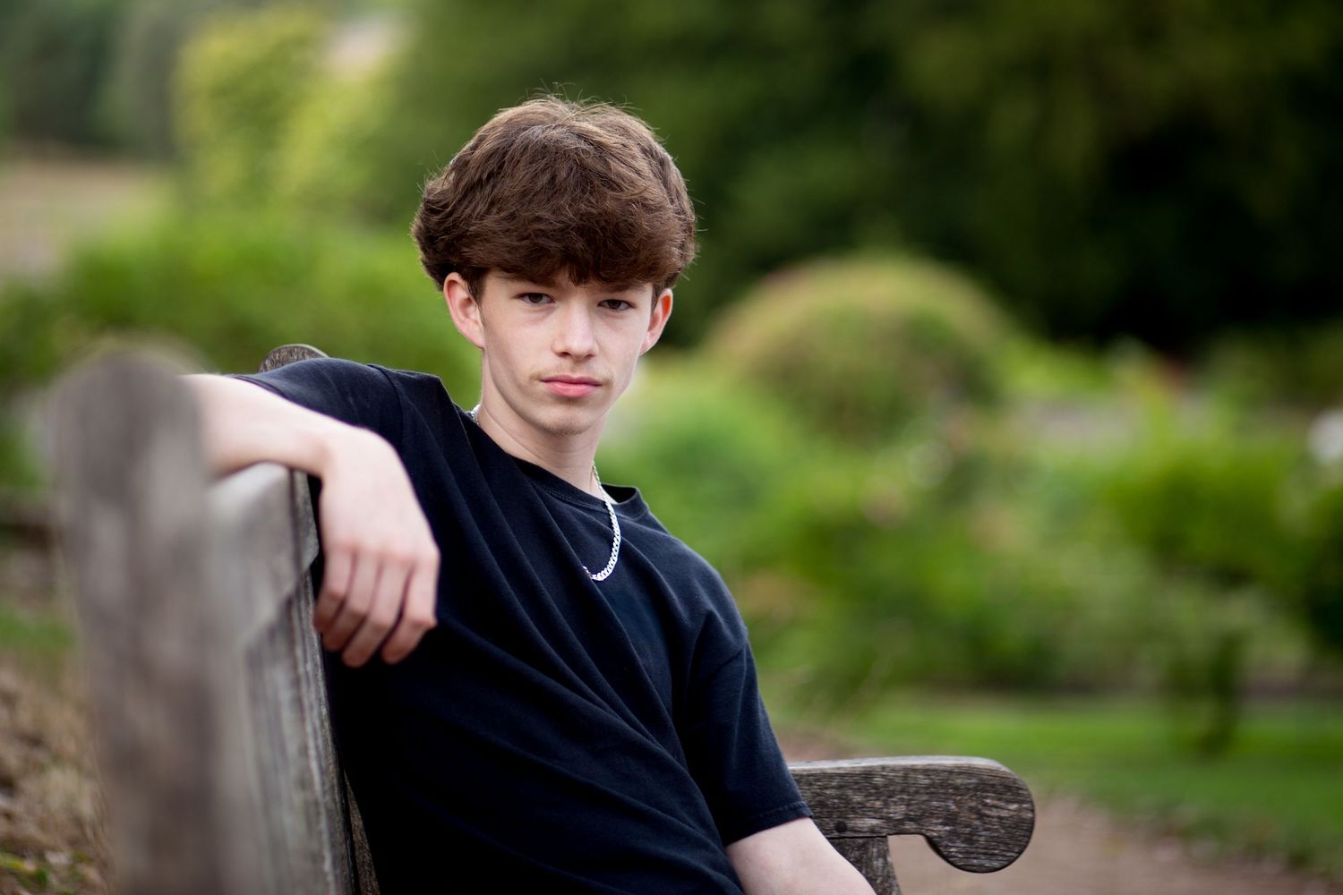 Teenage boy sitting on a wooden bench in a Bristol park, natural portrait.