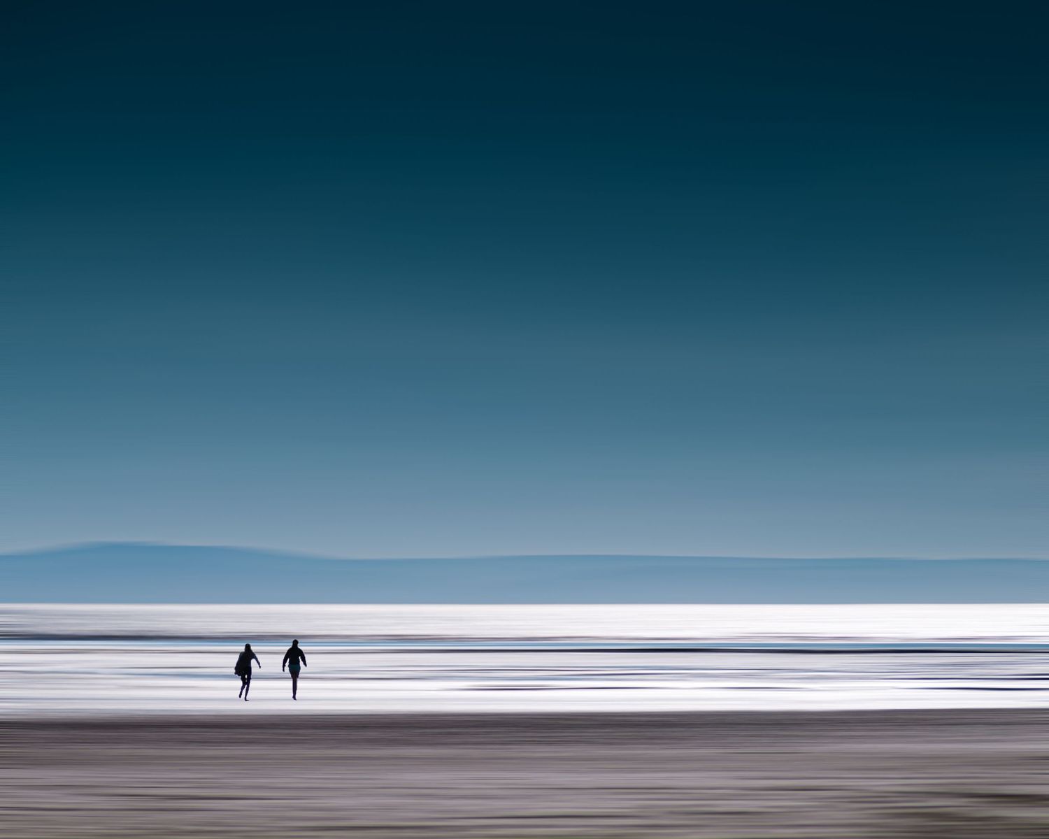 Two girls walking along Brean beach in Somerset at low tide with distant horizon.