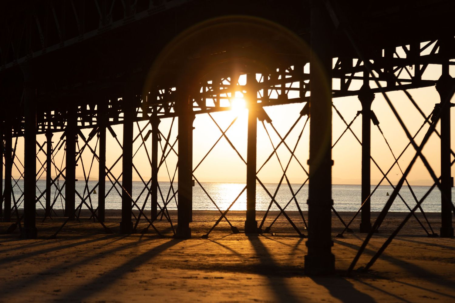 Sun setting through the supports of Weston-super-Mare pier, coastal photography Somerset.