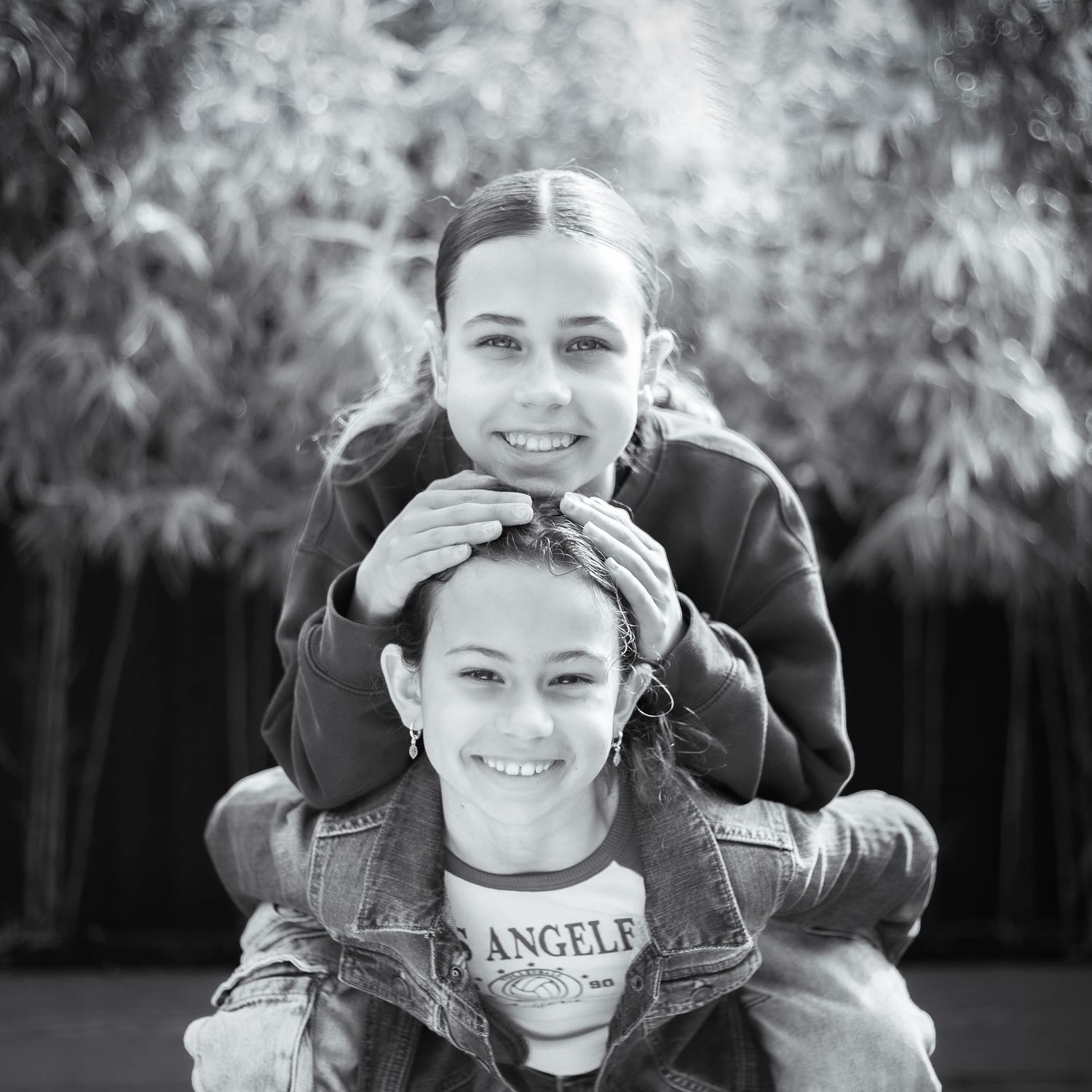 Black and white portrait of two siblings outdoors, smiling and stacked in playful pose.