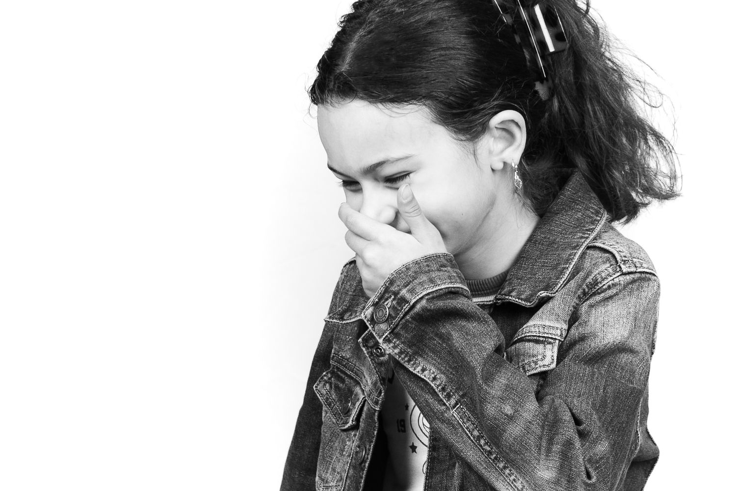 Black and white portrait of a young girl smiling shyly in a denim jacket.