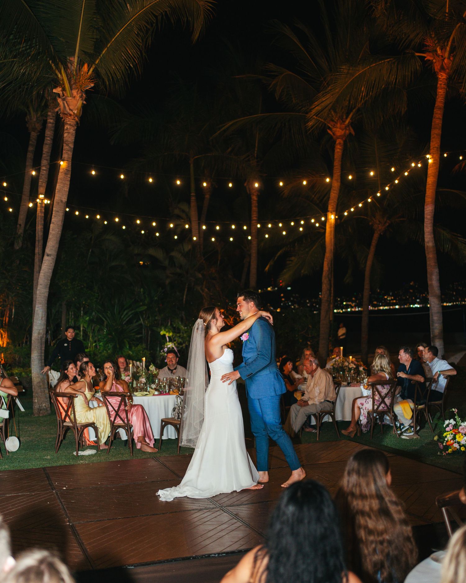 Newlyweds share their first dance under string lights at an elegant outdoor tropical evening reception.