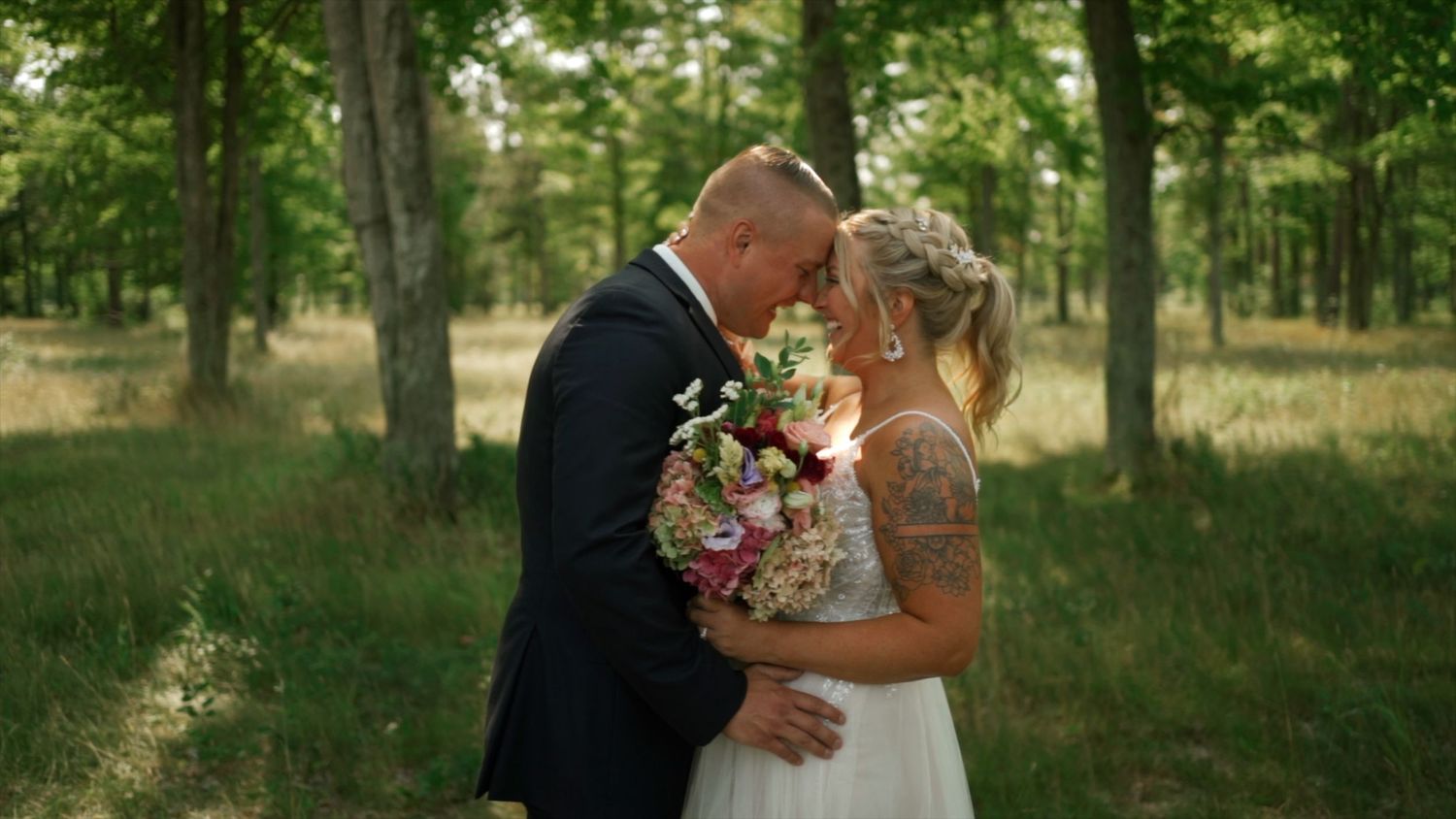 Bride and groom sharing an intimate moment in a forest, bride holding a vibrant floral bouquet.